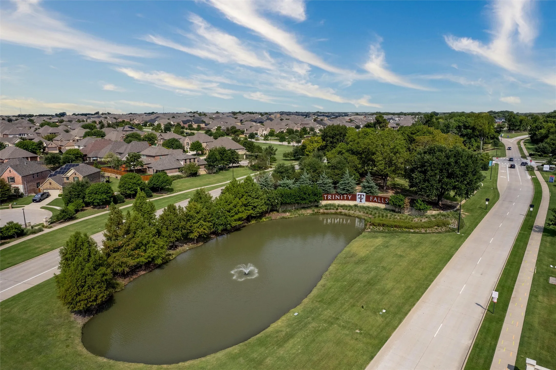 Residential community with an expansive green space, a decorative water feature, and mature trees