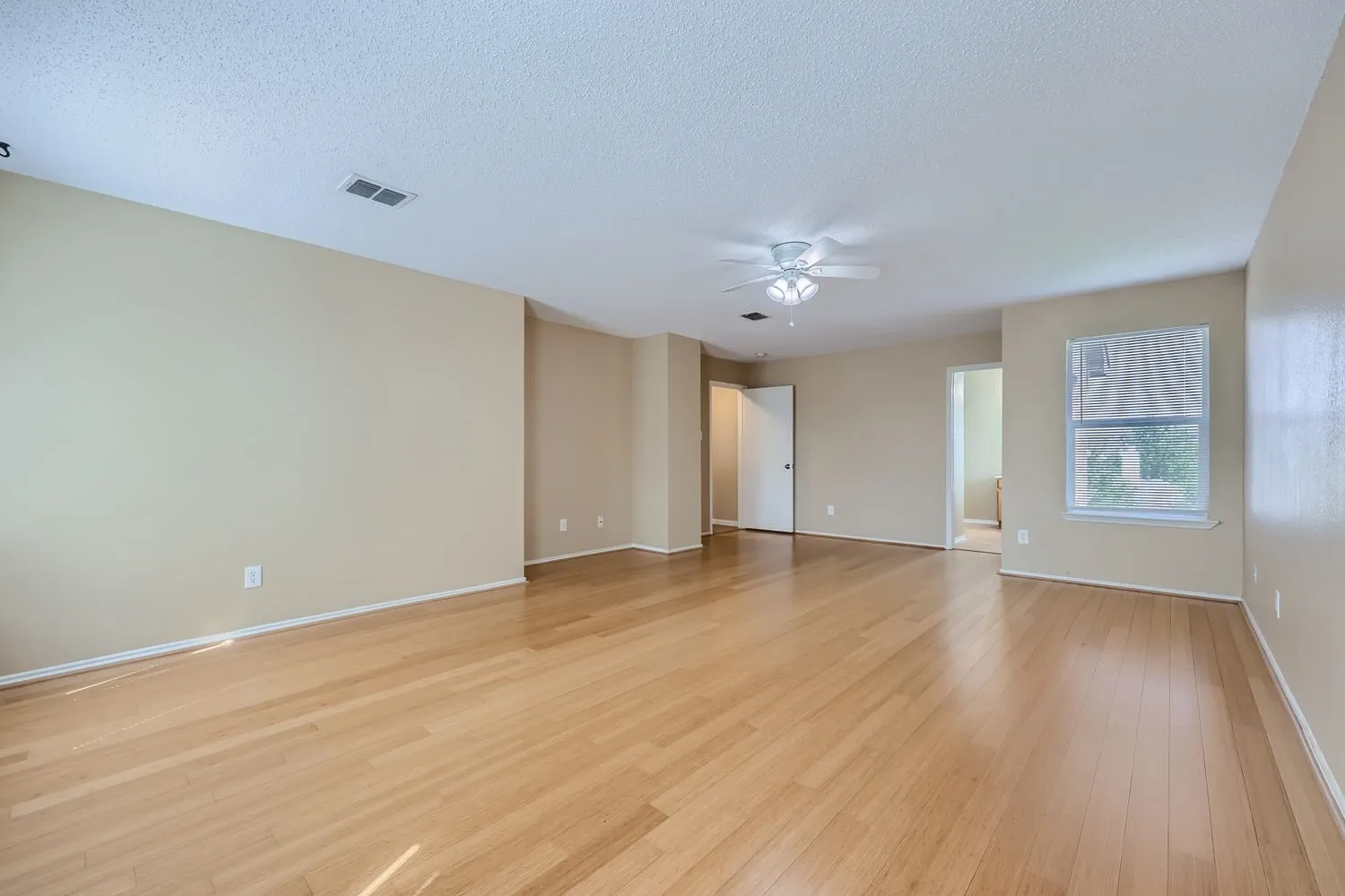 Spacious room featuring wood-finish flooring, a ceiling fan, and a window for natural light