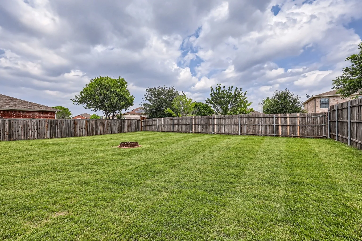 Expansive grassy yard with full privacy fencing and a built-in fire pit