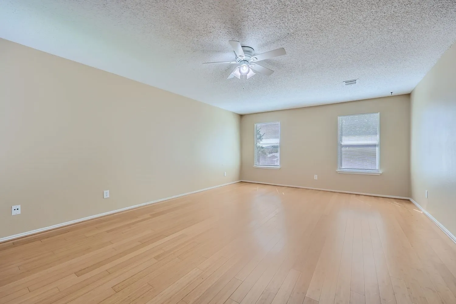 Spacious room featuring wood-finish flooring, neutral-toned walls, and a ceiling fan