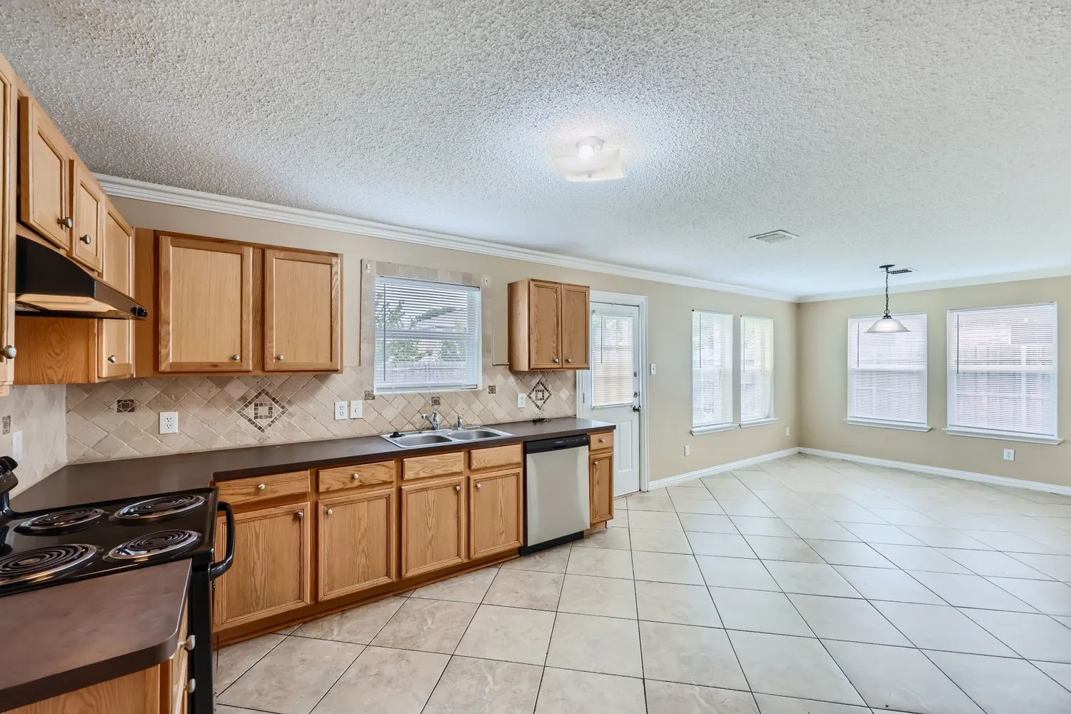 Full kitchen featuring wood cabinetry, stainless steel dishwasher, and patterned tile backsplash