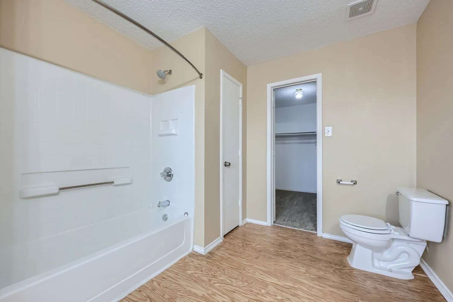 Tub/shower combination with chrome fixtures, wood-finish flooring, and a white toilet