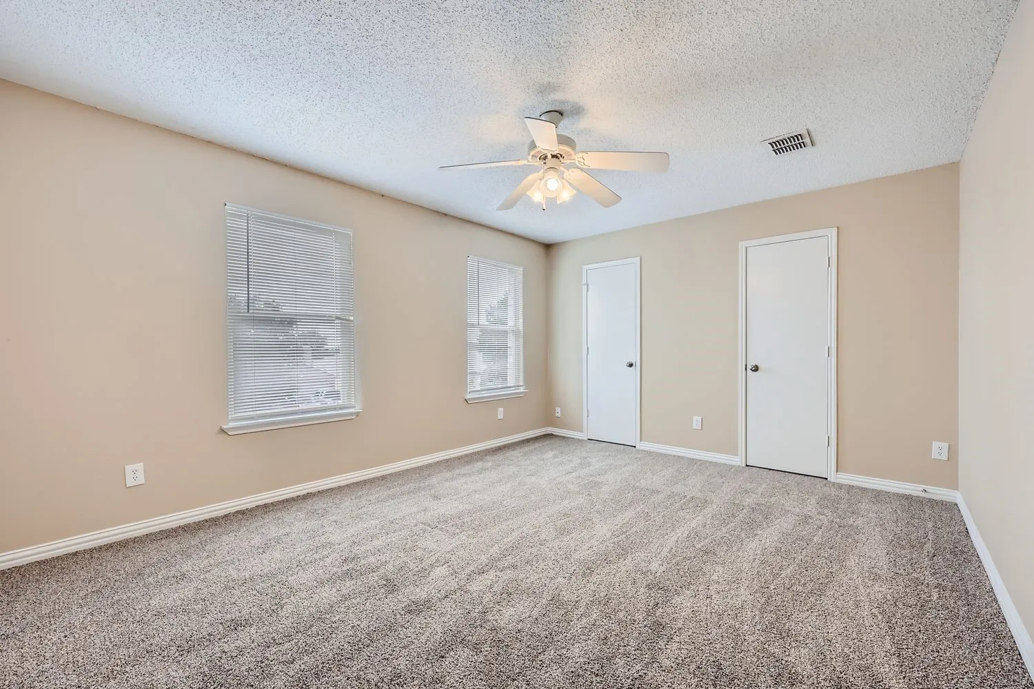 Neutral wall tones, two windows with blinds, two interior doors, gray carpet, and ceiling fan with light fixture