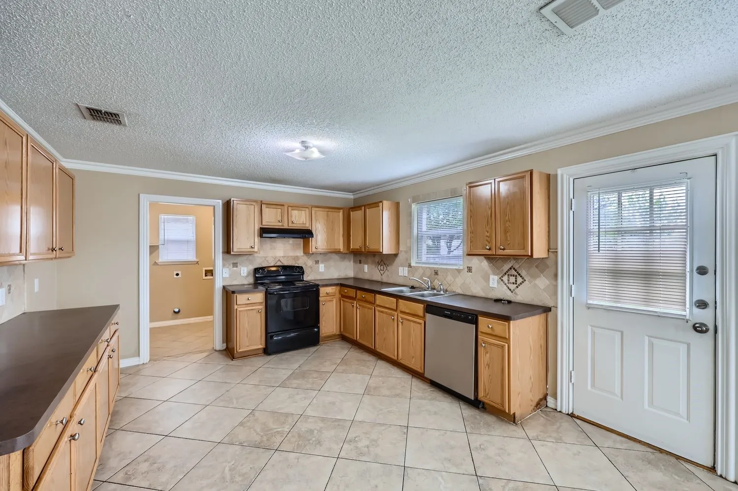 Kitchen with light wood-finish cabinetry, dark countertops, and a tile backsplash
