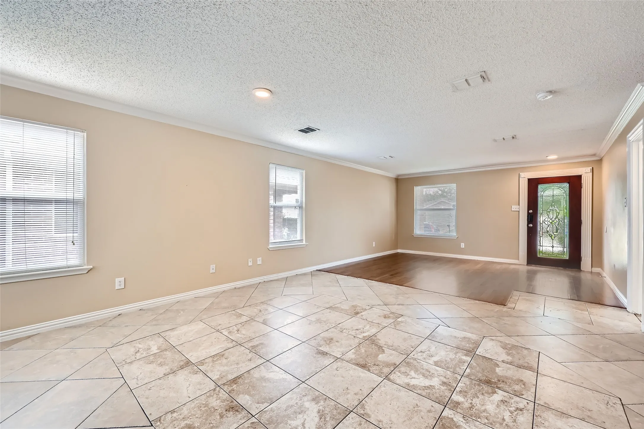 Expansive room featuring mixed flooring with large square tiles and wood-finish sections, multiple windows, recessed lighting, and a decorative glass-paneled entry door