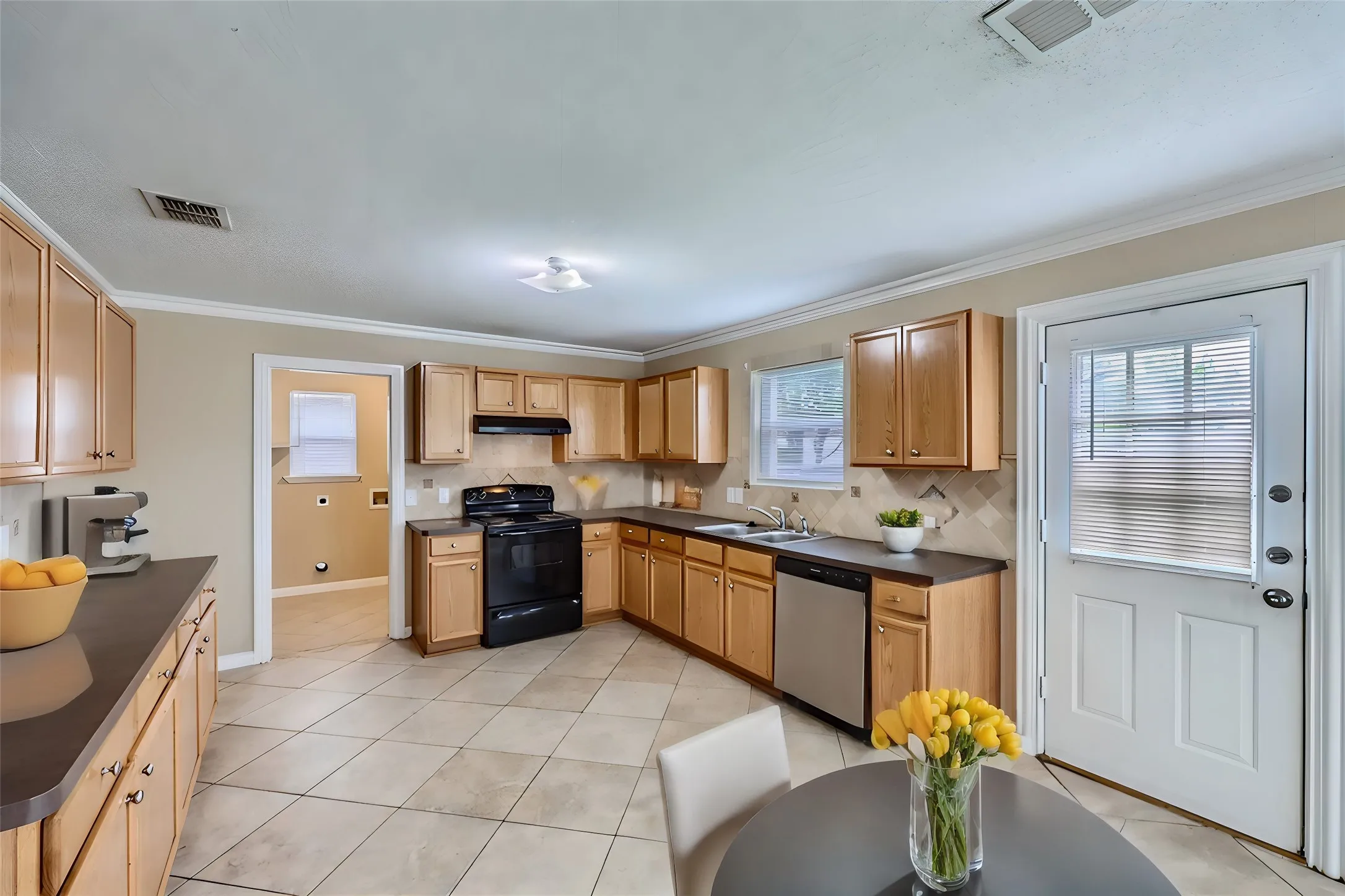 Kitchen featuring wood cabinetry, dark countertops, tiled flooring, and stainless steel dishwasher
