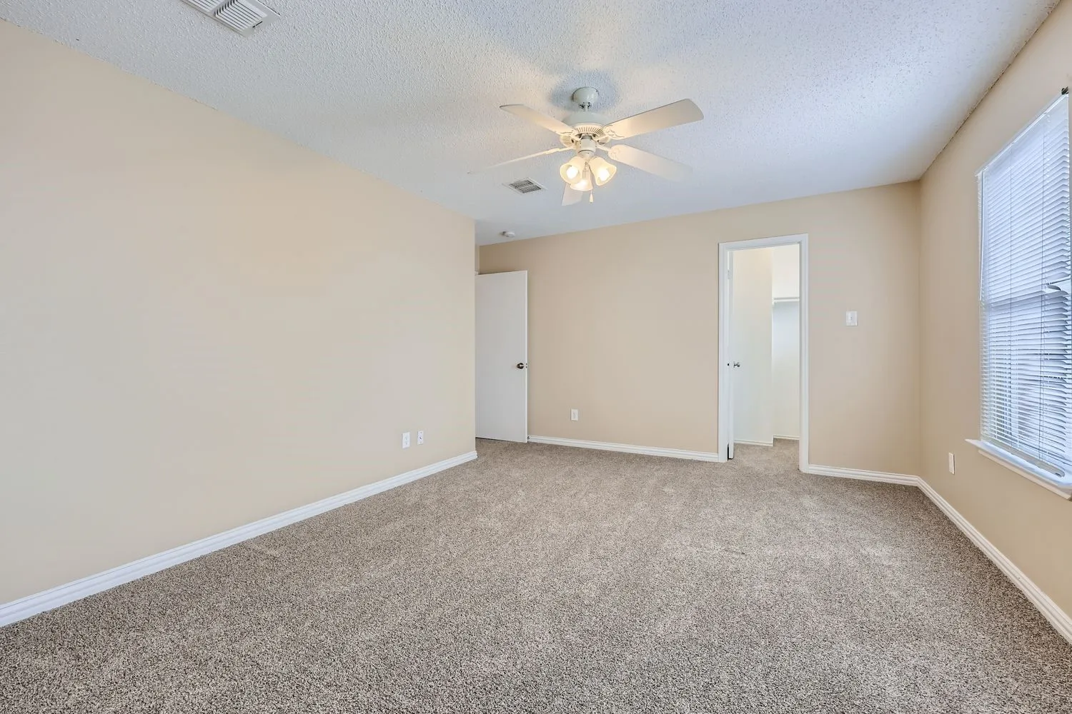Carpeted flooring, neutral wall tones, ceiling fan with light fixture, window with blinds, and a built-in closet with shelving