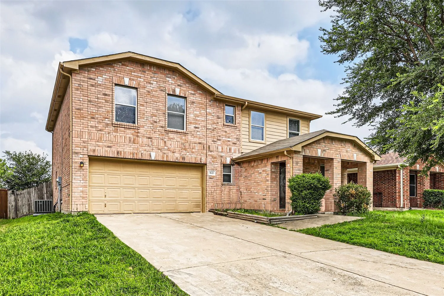 Brick exterior with a covered entry, attached garage, and concrete driveway