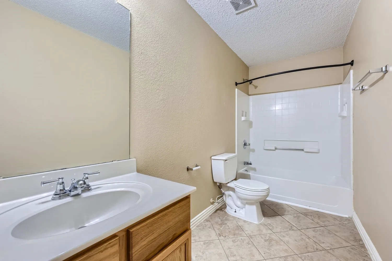 Bathroom featuring a light-toned vanity with an integrated sink, polished chrome faucet, a large wall-mounted mirror, a white toilet, and a white tub/shower combination with a curved shower rod