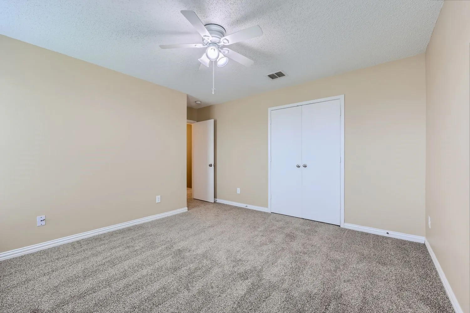 Neutral tone wall paint, textured carpet flooring, ceiling fan with integrated lighting, and bi-fold closet doors