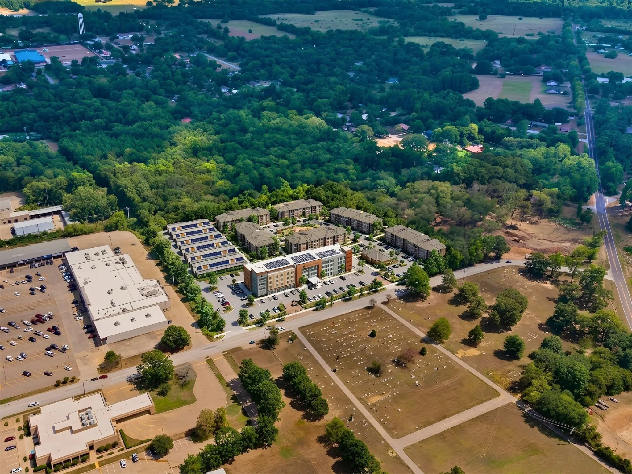 Aerial perspective showcasing a mixed-use development with multi-story buildings, extensive parking areas, and surrounding green spaces