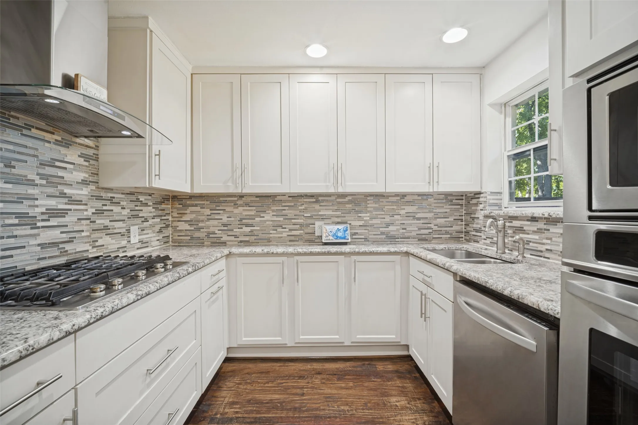 Modern kitchen featuring white cabinetry, stainless steel appliances, a tile backsplash, light-toned countertops, and wood-finish flooring