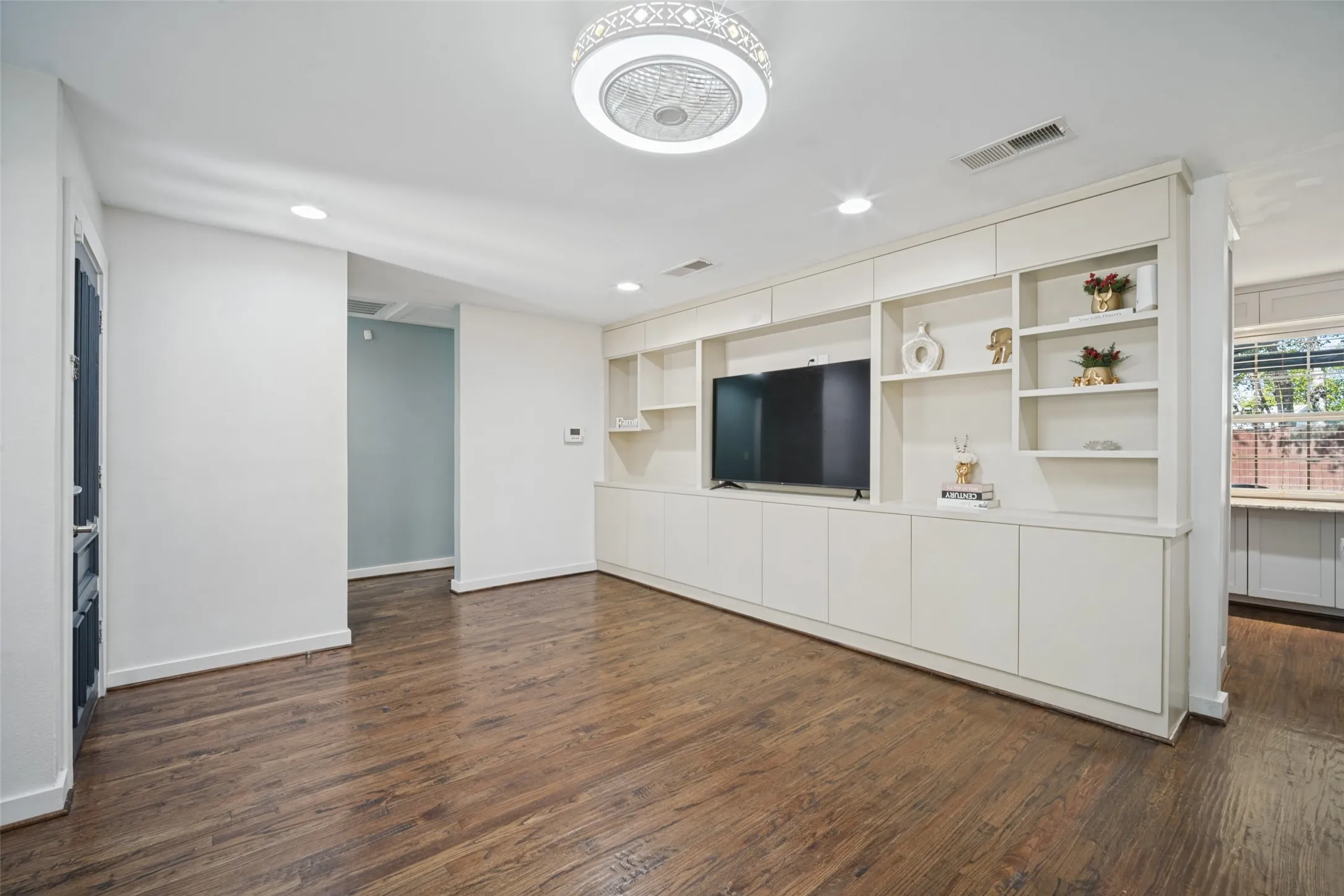 Wood-finish flooring, white walls, and a built-in entertainment center with integrated shelving
