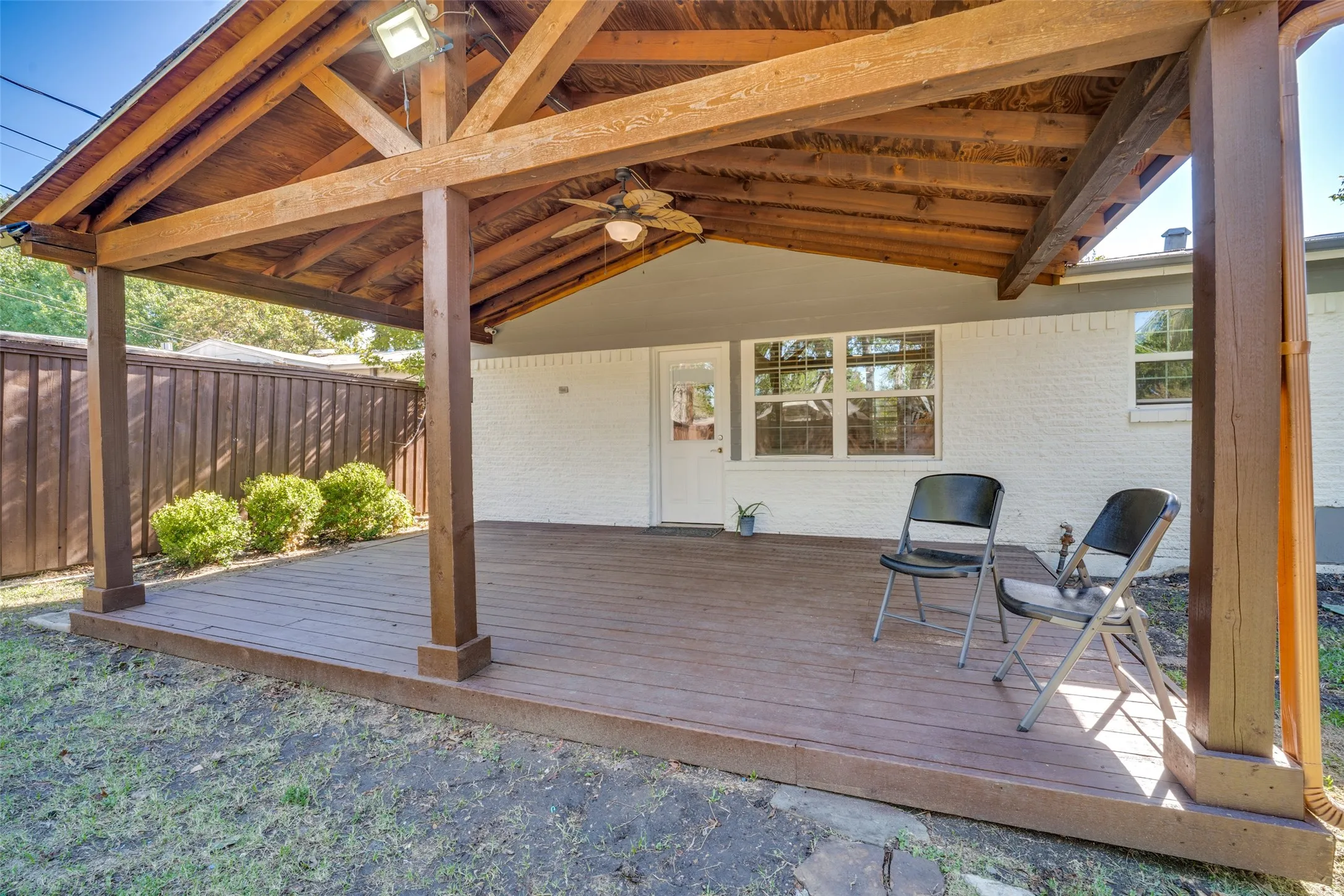 Expansive covered patio with exposed wood beams, composite decking, and a ceiling fan