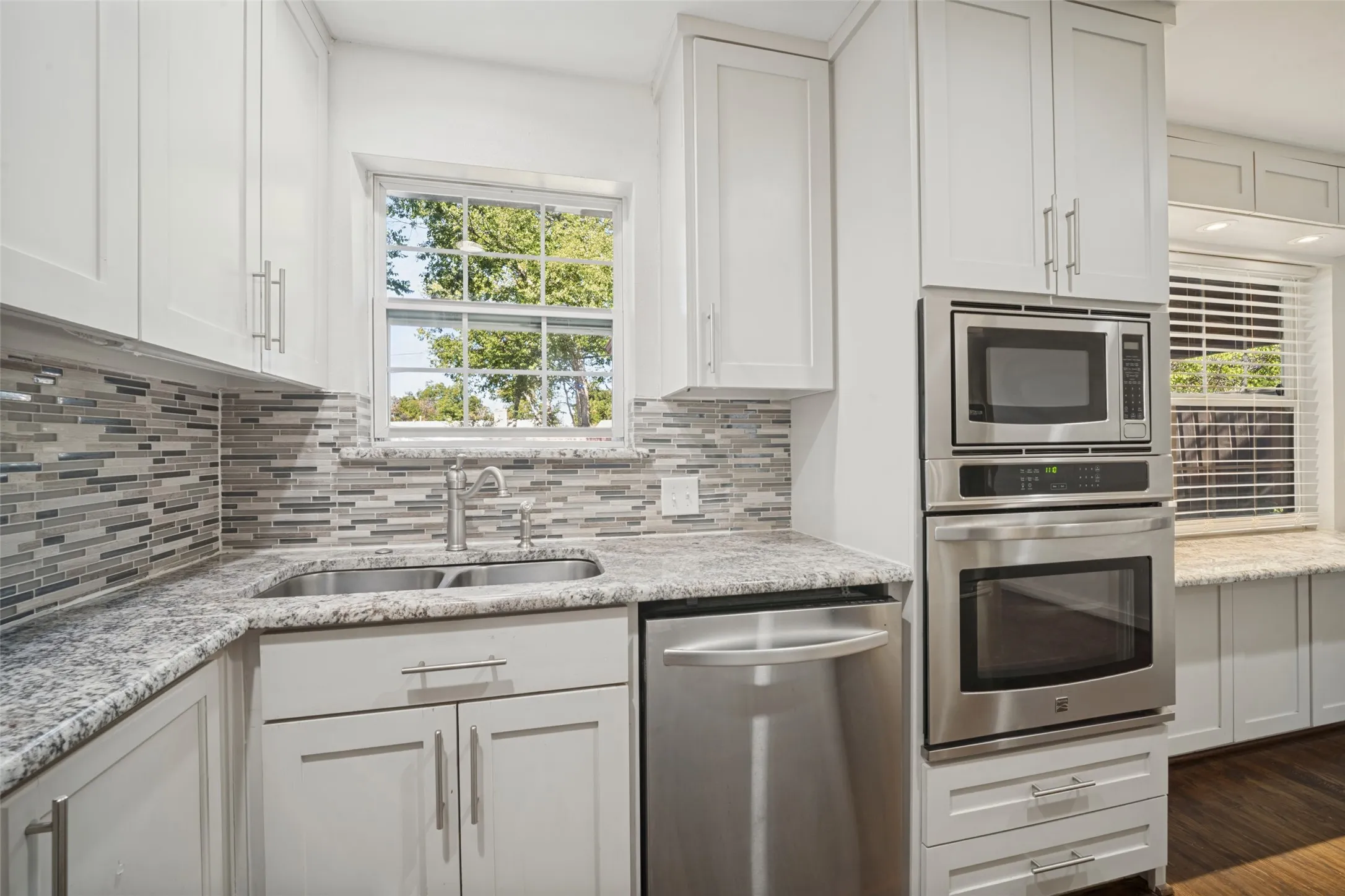 White cabinetry, stainless steel appliances, mosaic tile backsplash, double basin sink, and ample countertop space