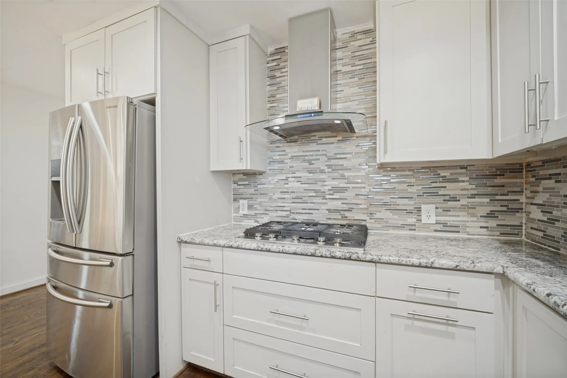 White shaker-style cabinetry with chrome hardware, stone countertops, gas range, and a mosaic tile backsplash