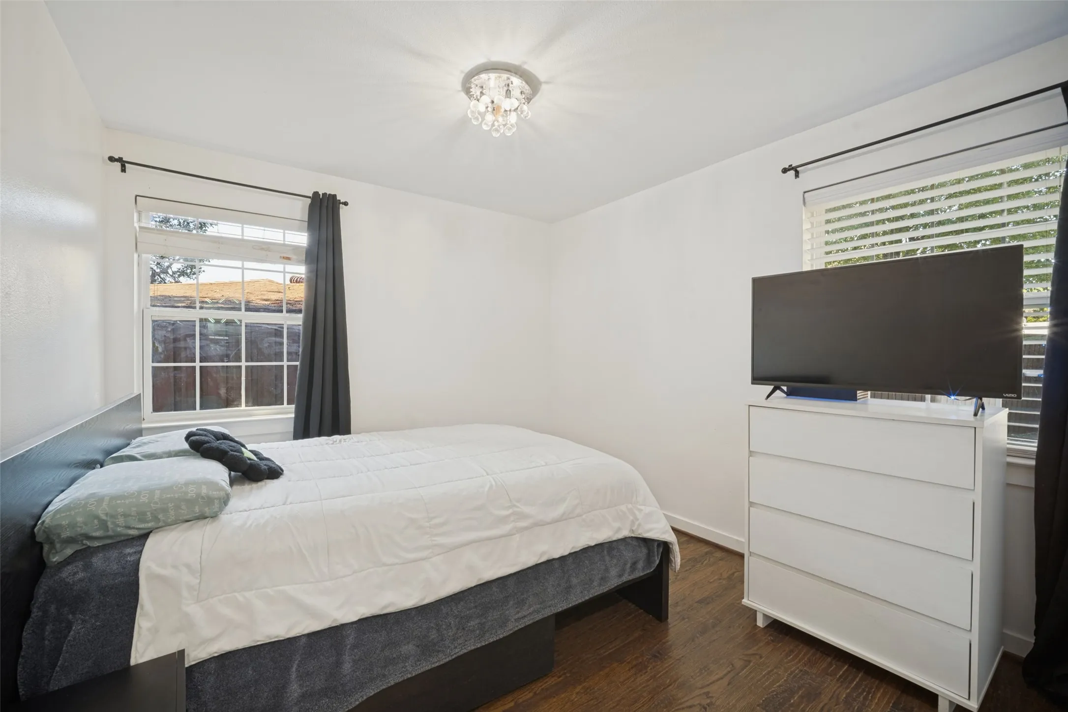 Hardwood-style flooring, white walls, two window openings, and a crystal-style flush mount light fixture