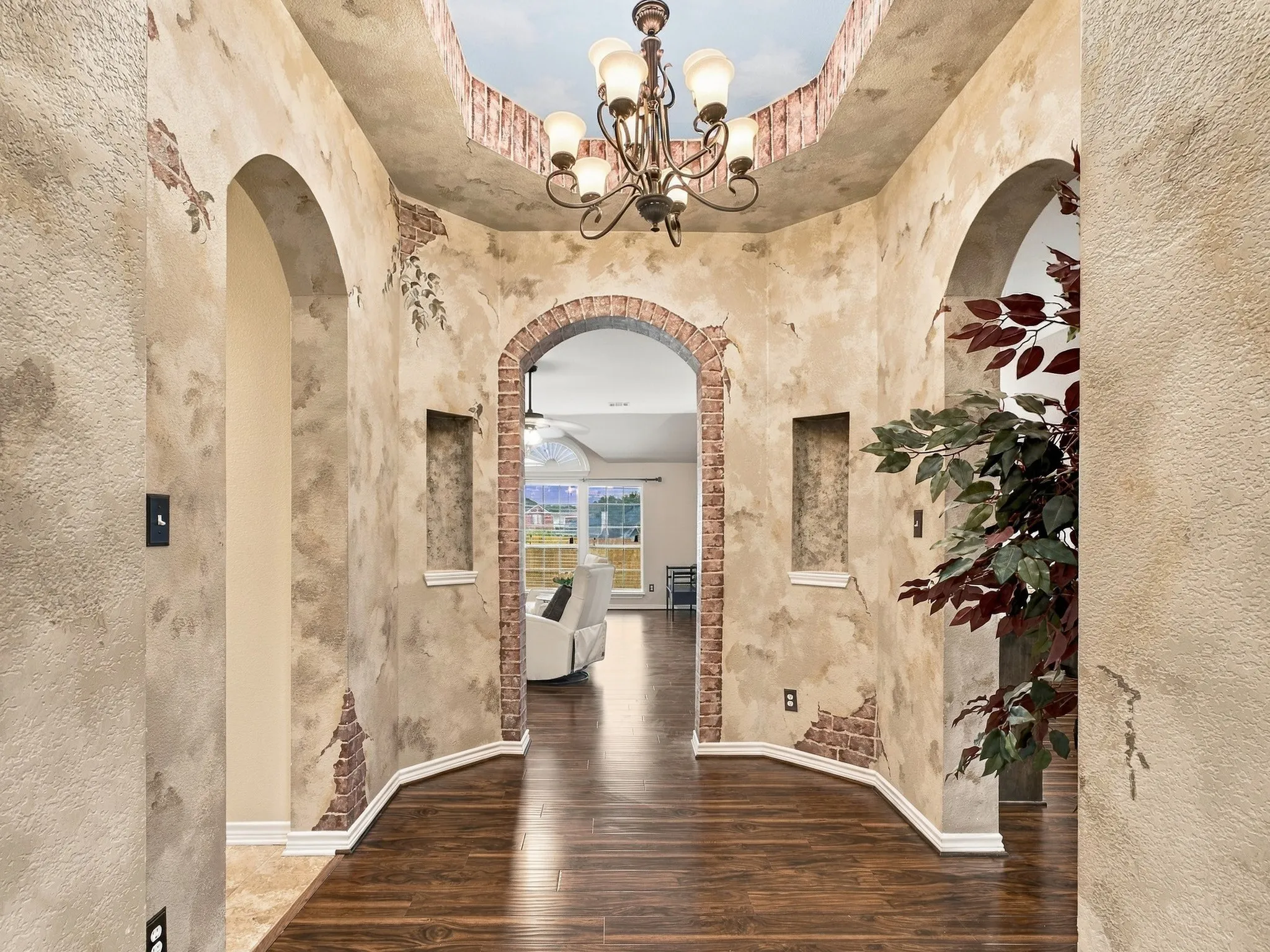Arched doorways with brick detailing, recessed wall niches, wood-finish flooring, and an ornate chandelier
