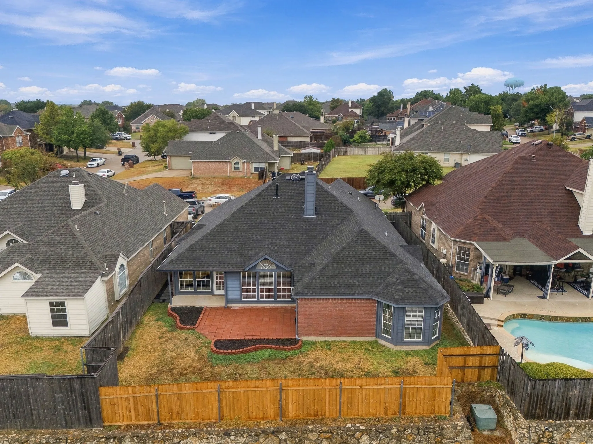 Backyard featuring a red brick patio, contrasting blue siding, and a wood privacy fence