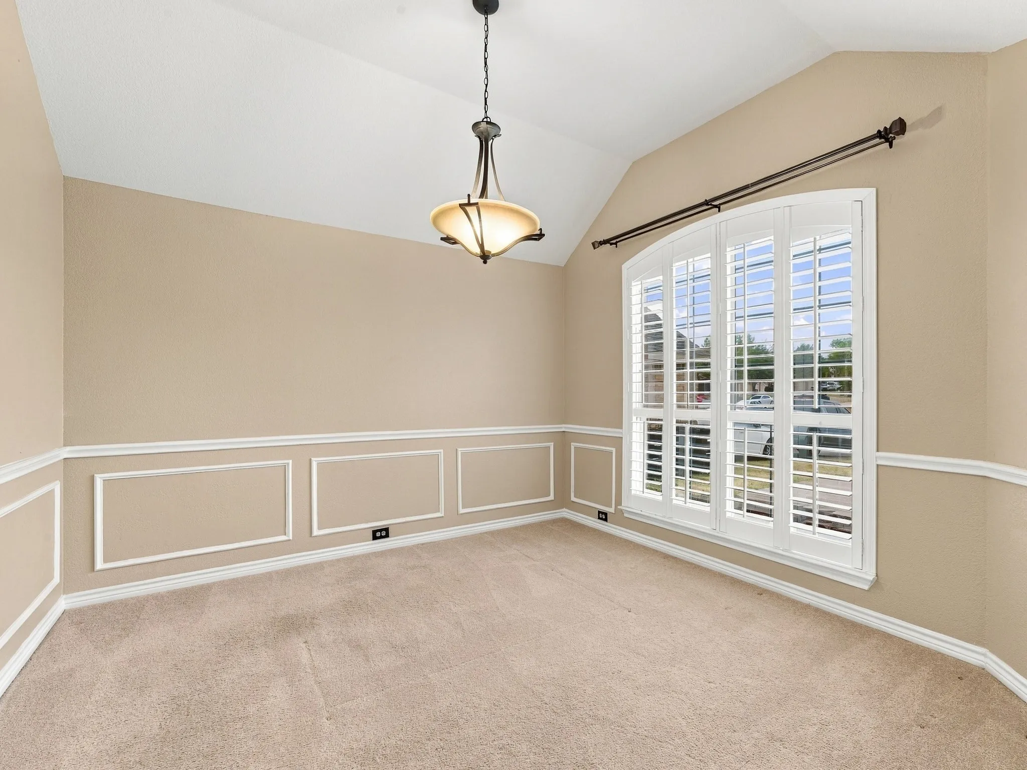 Vaulted ceiling with an attached light fixture, arched window with plantation shutters, wainscoting with decorative molding, and carpeting