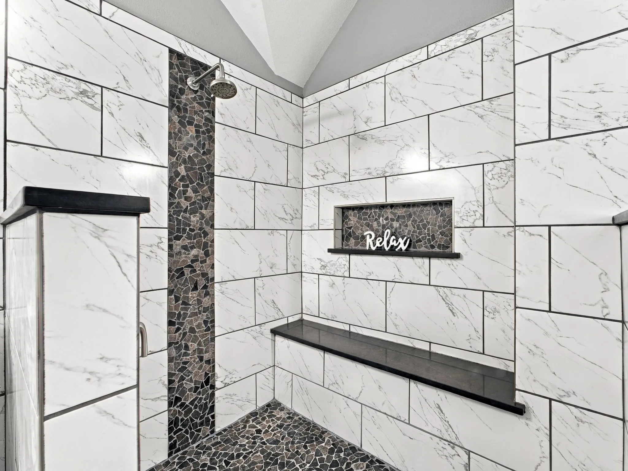 Spacious shower featuring white marble-look subway tile, a pebbled-tile floor, and a built-in shower niche