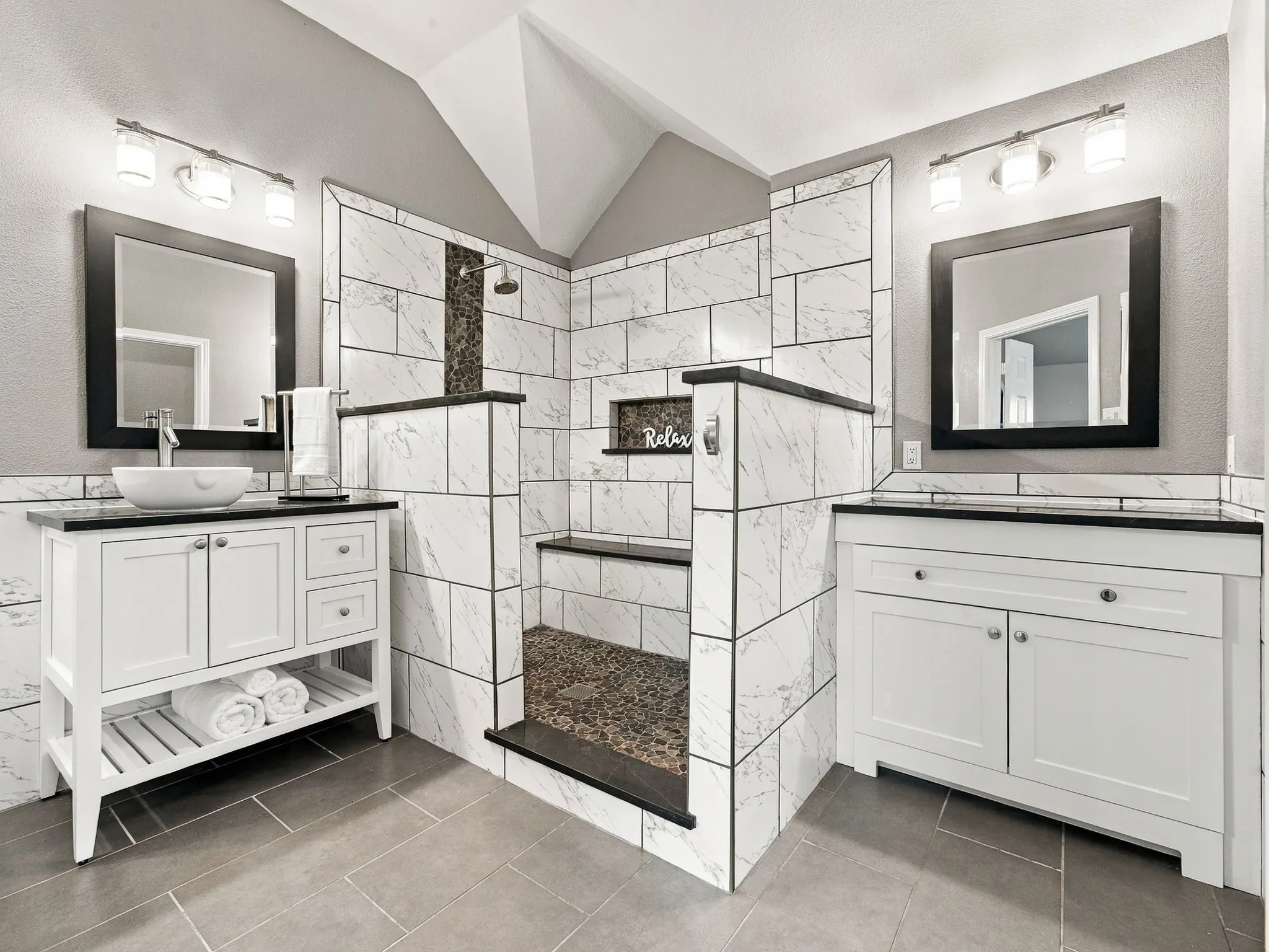 Walk-in shower with tiled walls and floor, dual vanities with vessel sinks, and grey tile flooring