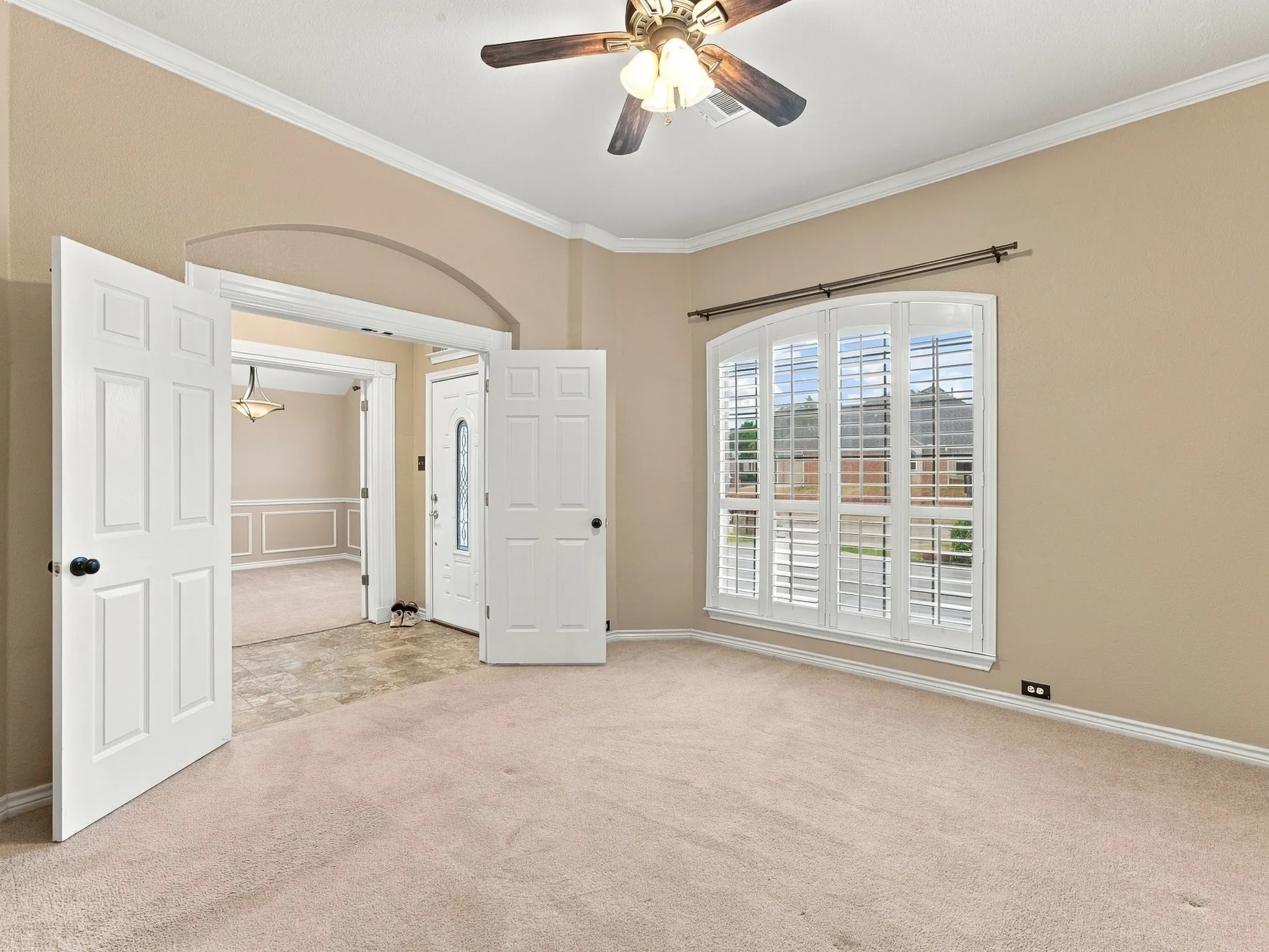Carpeted room featuring a ceiling fan, crown molding, and plantation shutters on arched windows
