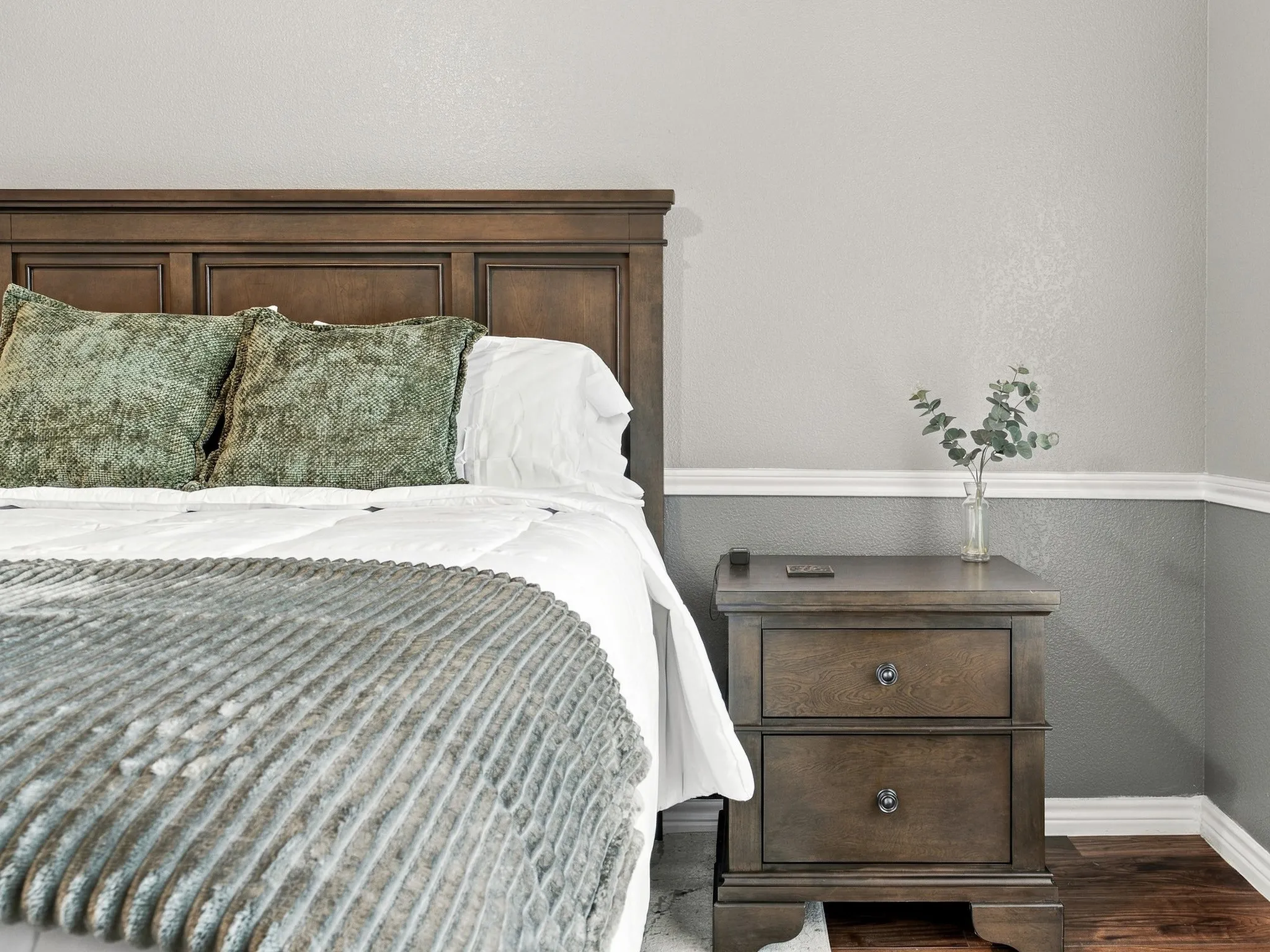 Paneled wood headboard, two-drawer nightstand with dark hardware, two-tone wall treatment, and white crown molding