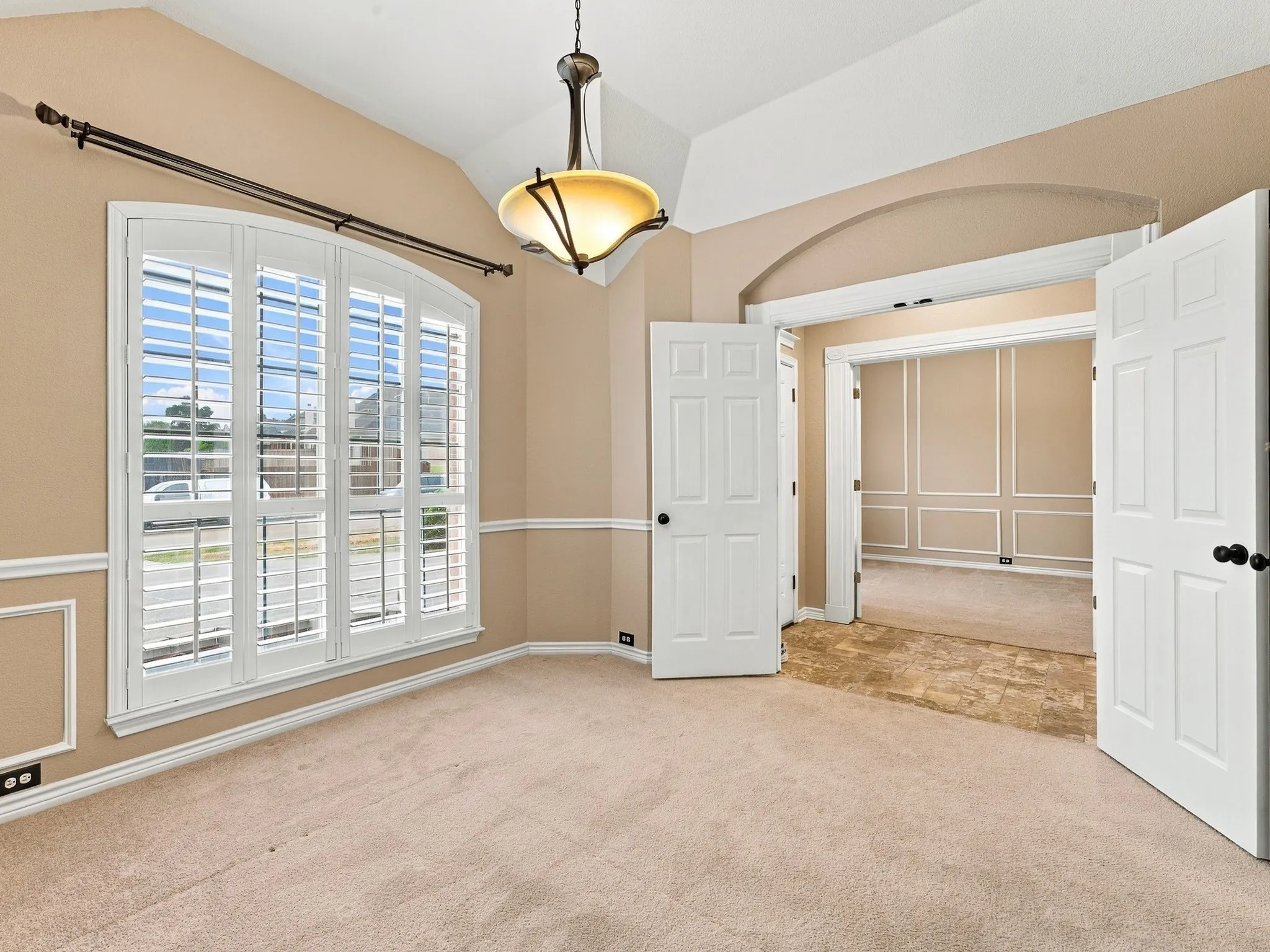 Arched window with plantation shutters, vaulted ceiling, and decorative molding