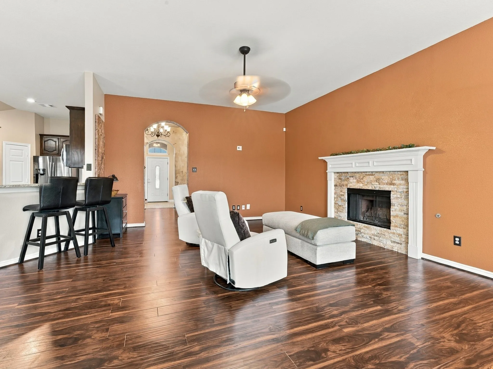 Spacious living area featuring wood-finish flooring, a stacked stone fireplace with a white mantel, and an arched entryway