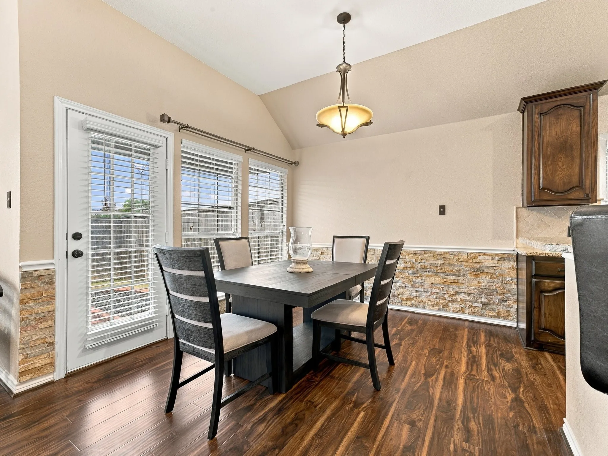 Vaulted ceiling with an attached light fixture, wood-finish flooring, stone-finish wainscoting, and a full-light exterior door