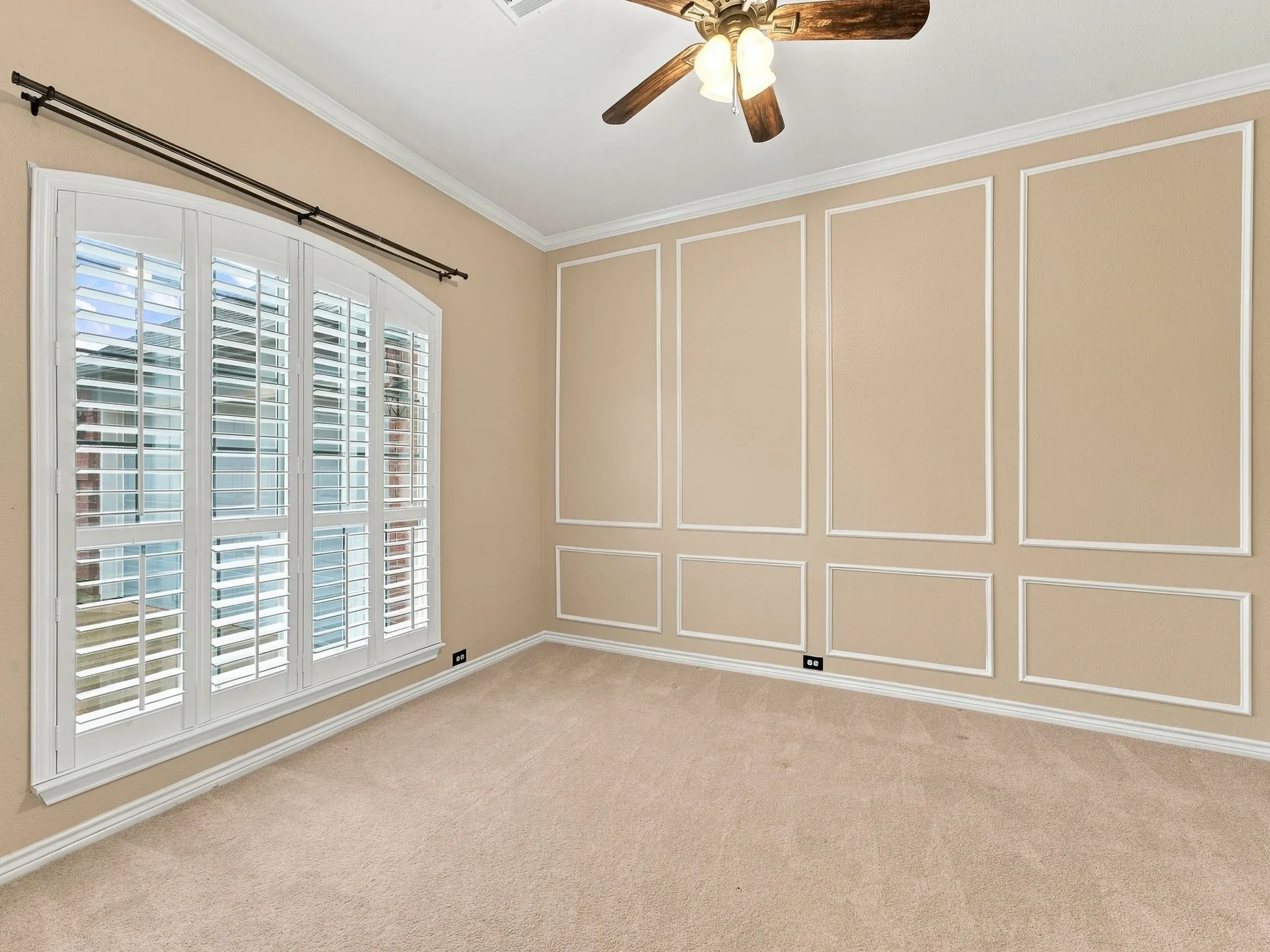 Arched window with plantation shutters, decorative wall molding, crown molding, ceiling fan with integrated lighting, and carpeted flooring