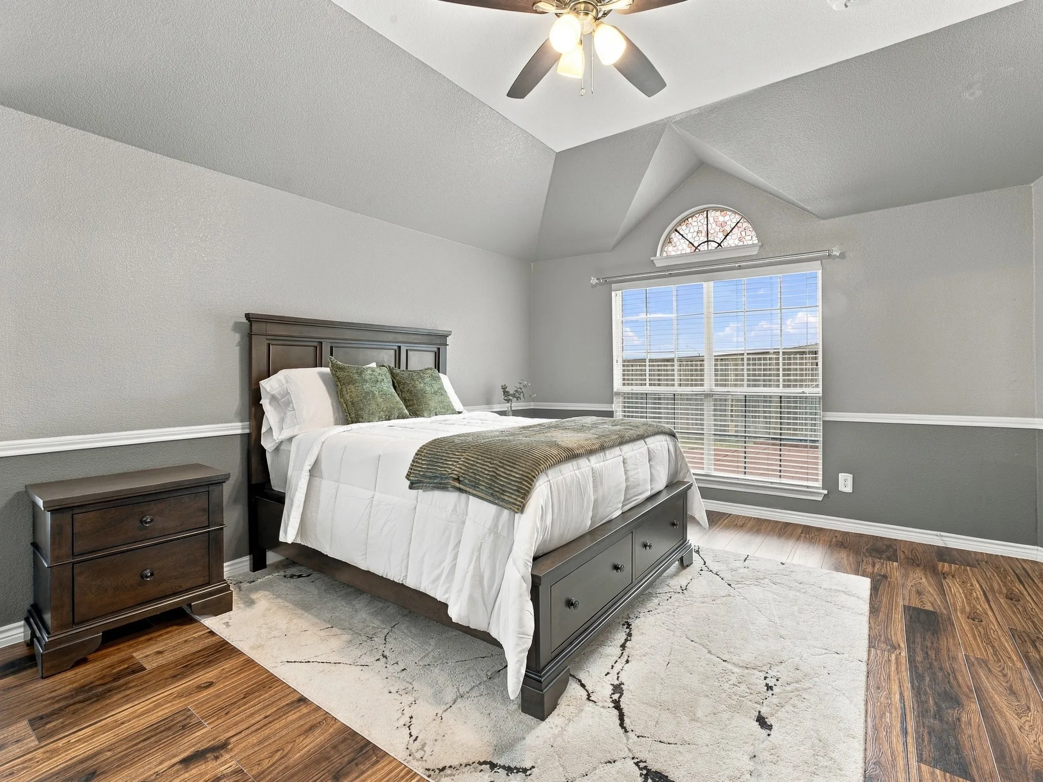 Vaulted ceiling with an arched window, wood-finish flooring, and crown molding