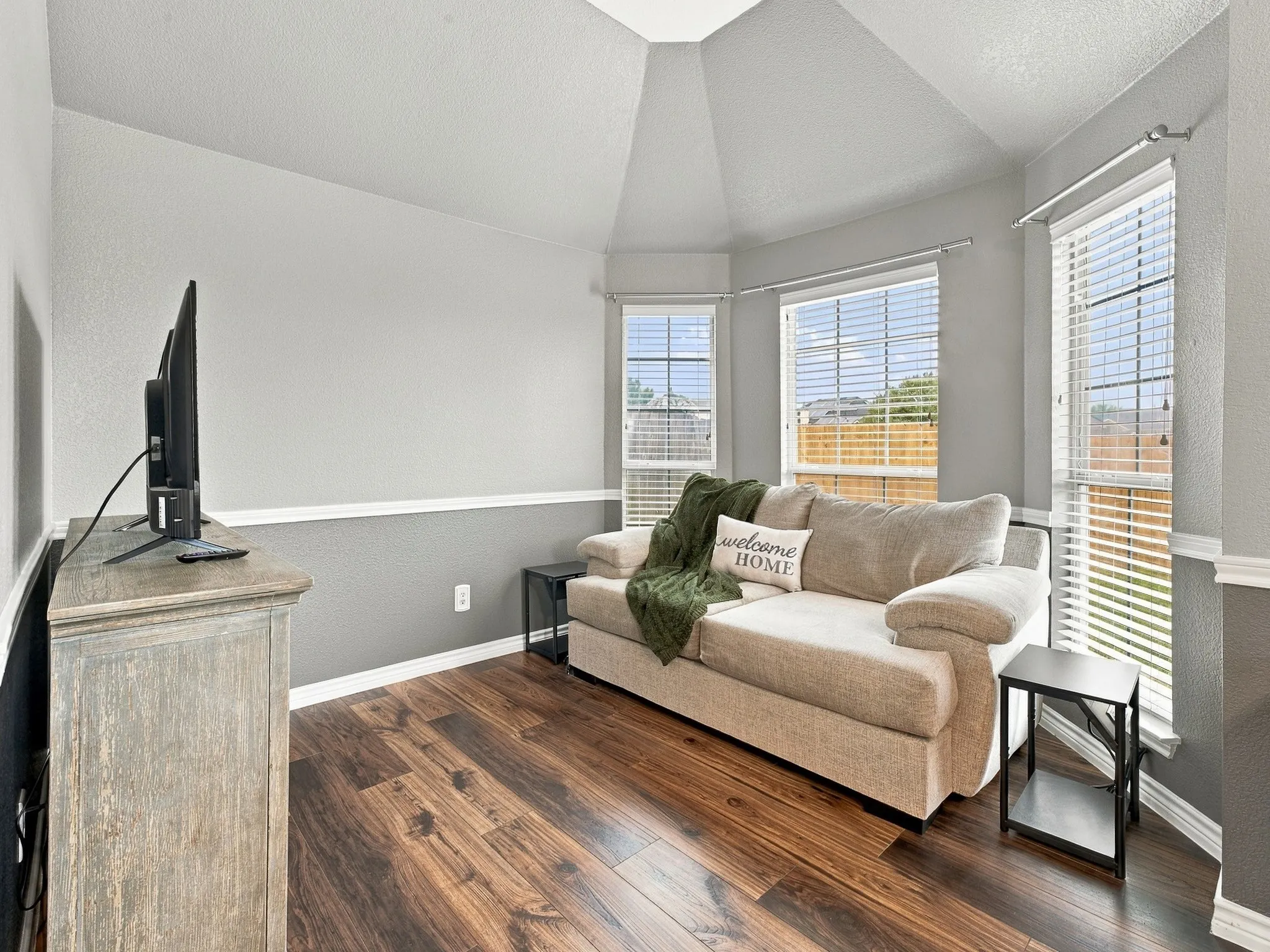 Wood-finish flooring with a two-tone wall treatment, vaulted ceiling, and multiple windows