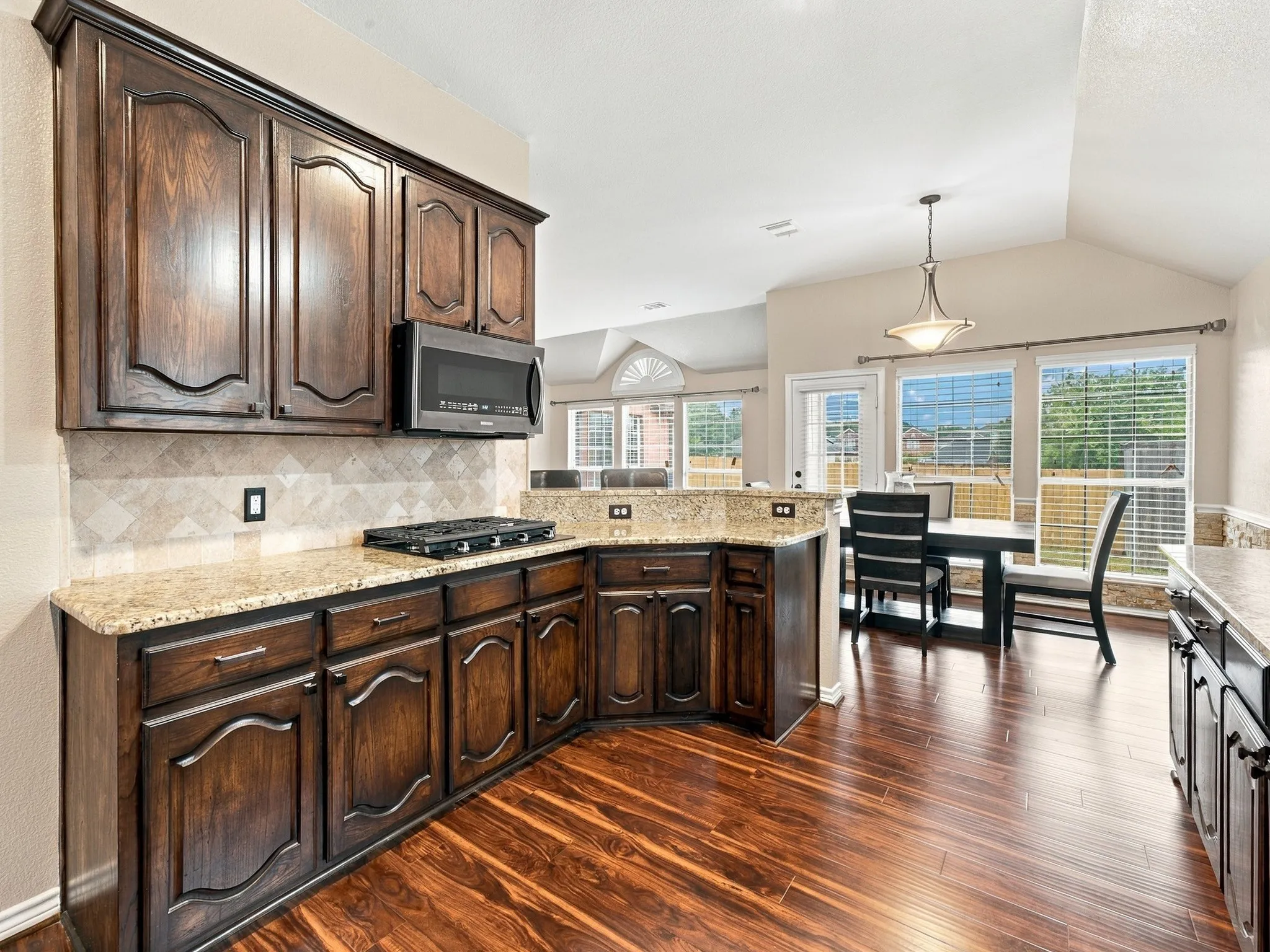 Dark wood-finish cabinetry, granite countertops, tile backsplash, built-in microwave, and wood-finish flooring
