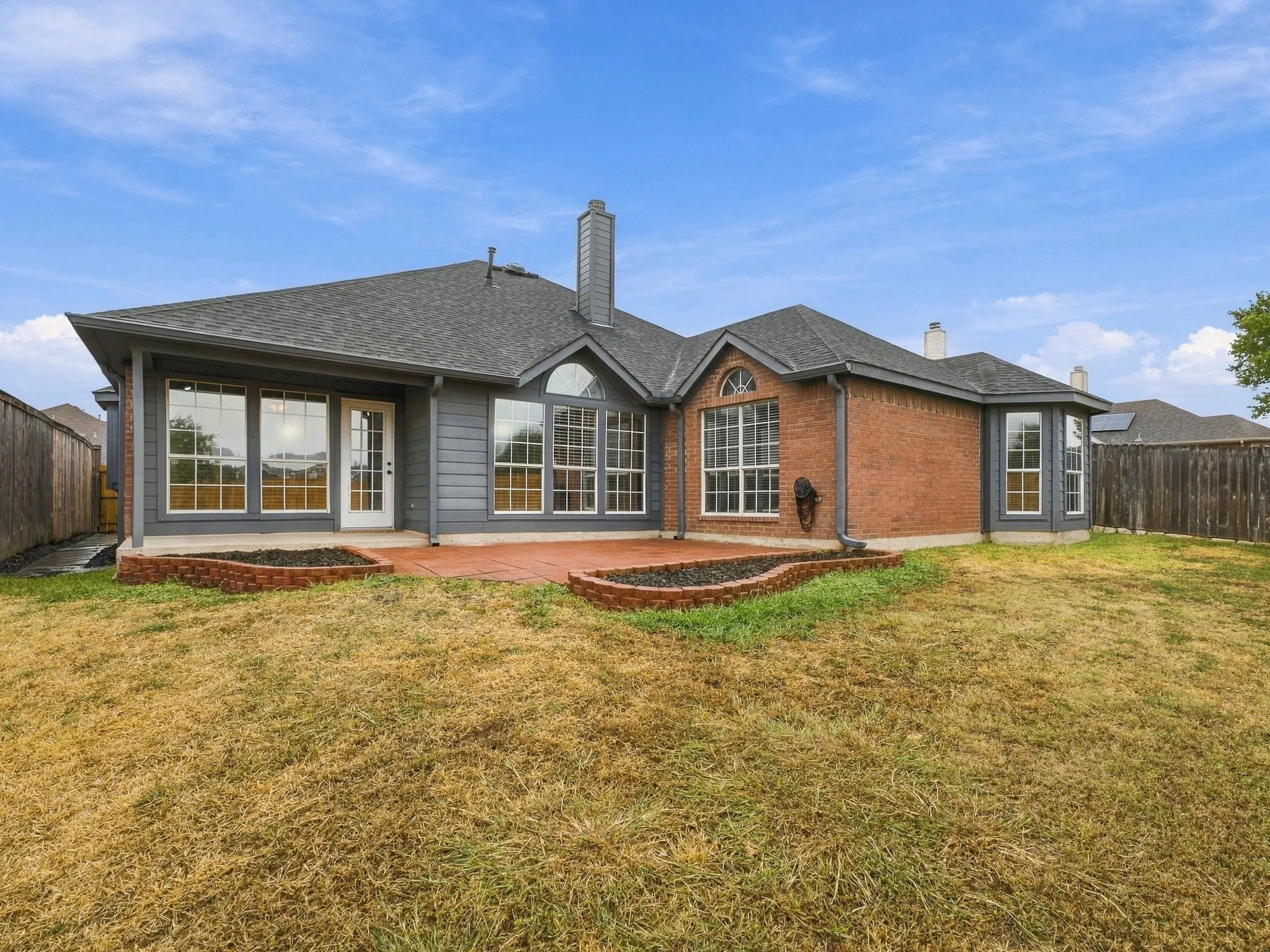Rear exterior featuring a covered patio, brick and siding facade, multiple large windows, and a fully fenced yard