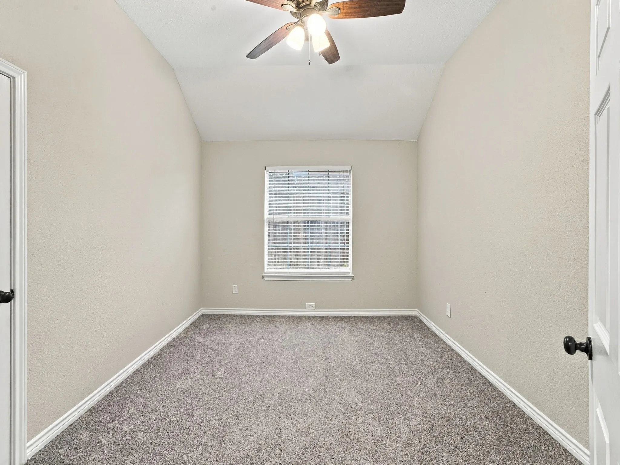 Vaulted ceiling, ceiling fan with light fixture, window with blinds, light gray carpet, and white trim molding