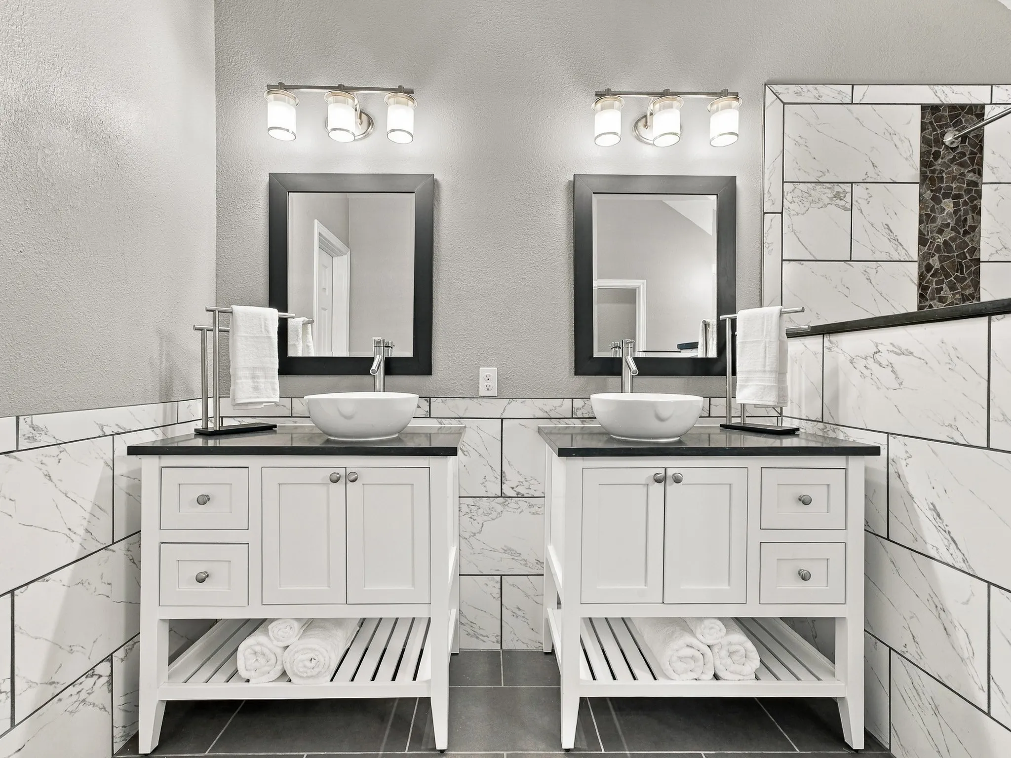 Dual white vanities with vessel sinks, dark countertops, and framed mirrors