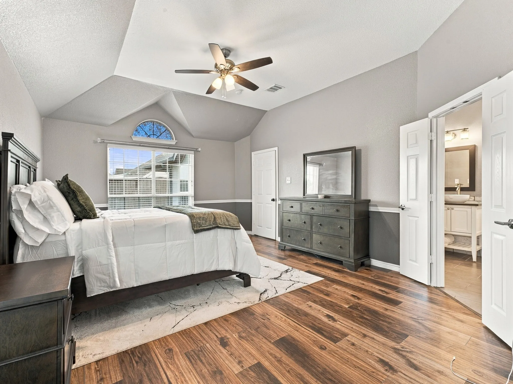 Vaulted ceiling with ceiling fan, wood-finish flooring, and a large window featuring an arched transom