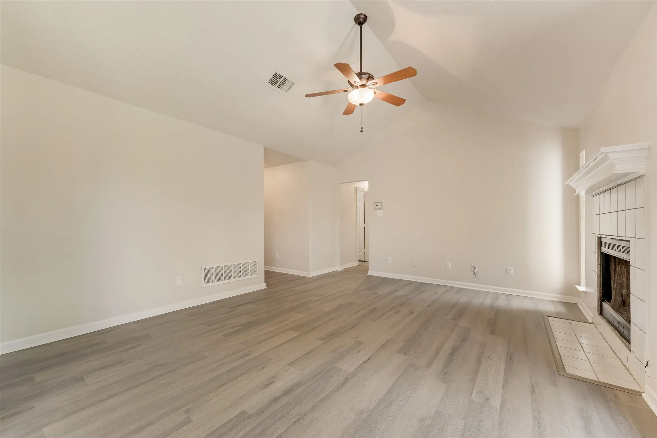 Vaulted ceiling, wood-finish flooring, white tiled fireplace with mantel, ceiling fan with integrated lighting