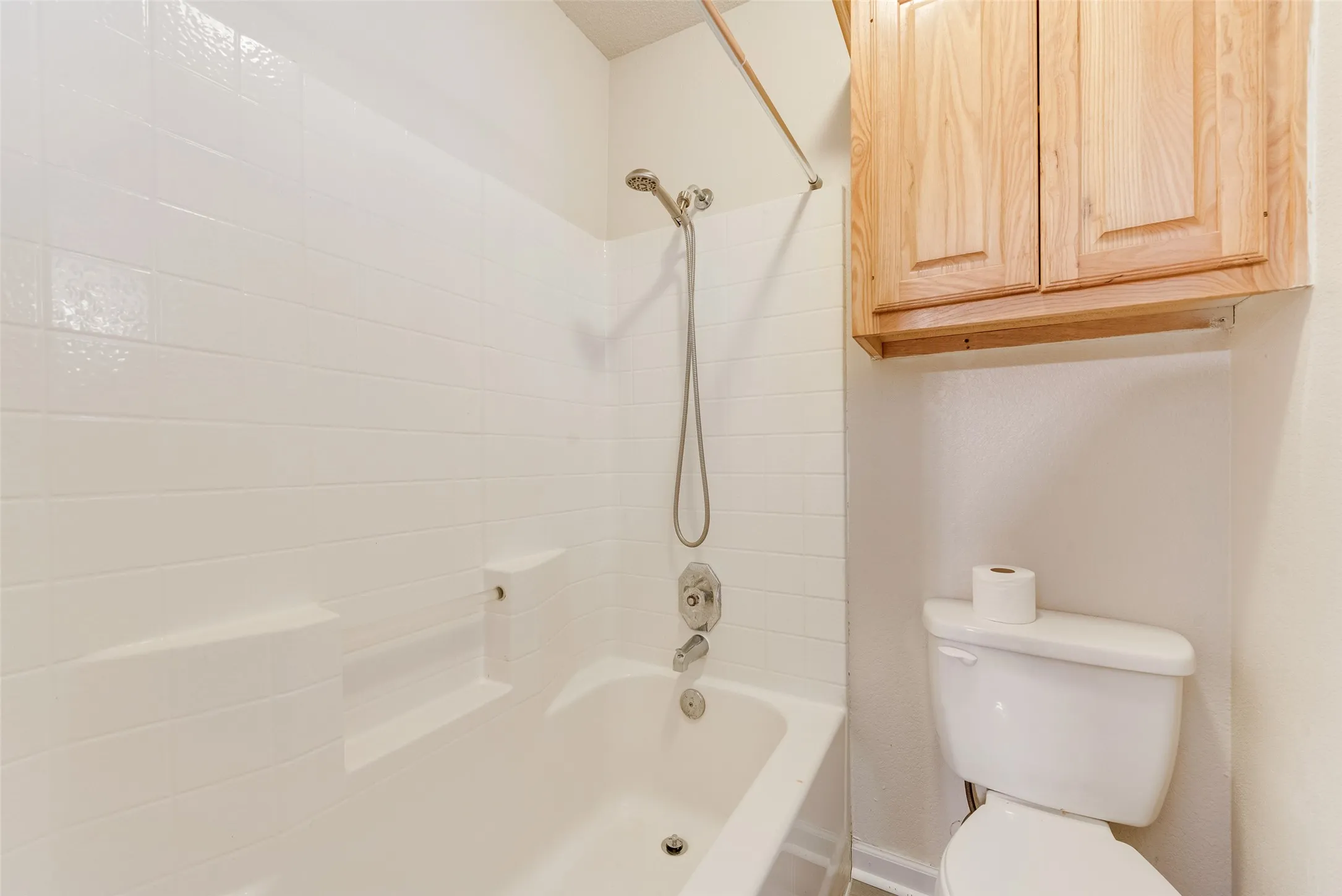 Bathtub with white tile surround, built-in shelving, and a handheld showerhead