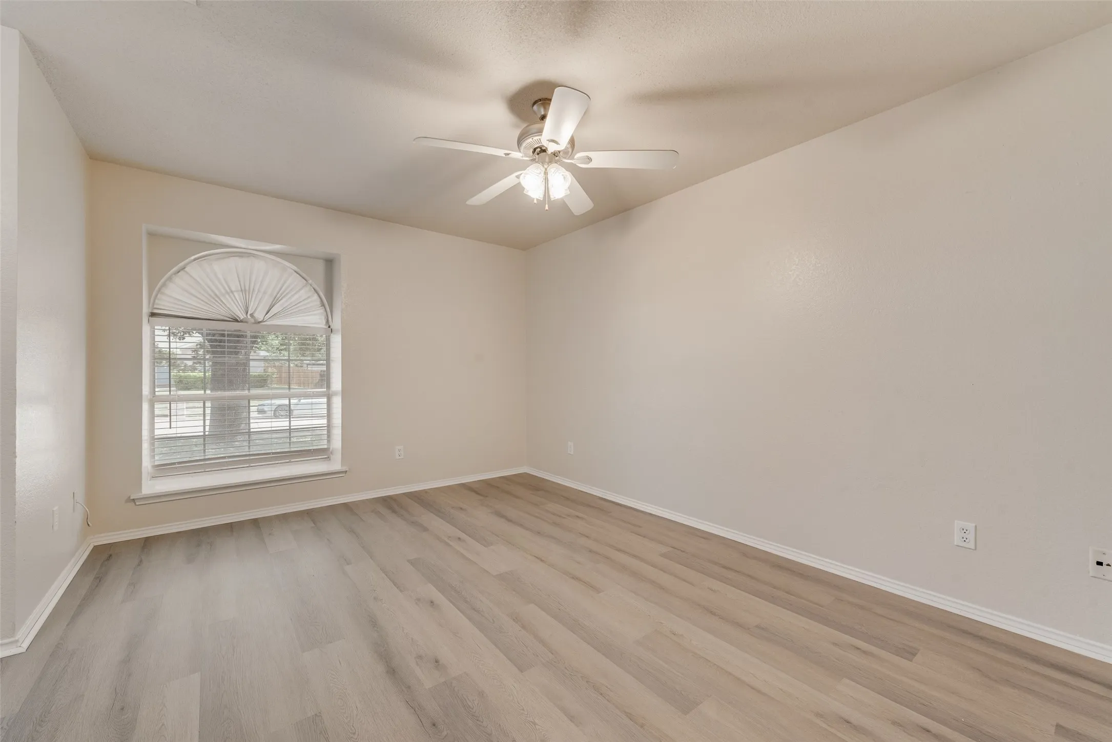 Arched window with blinds, wood-finish flooring, ceiling fan with light fixture, and neutral wall tones