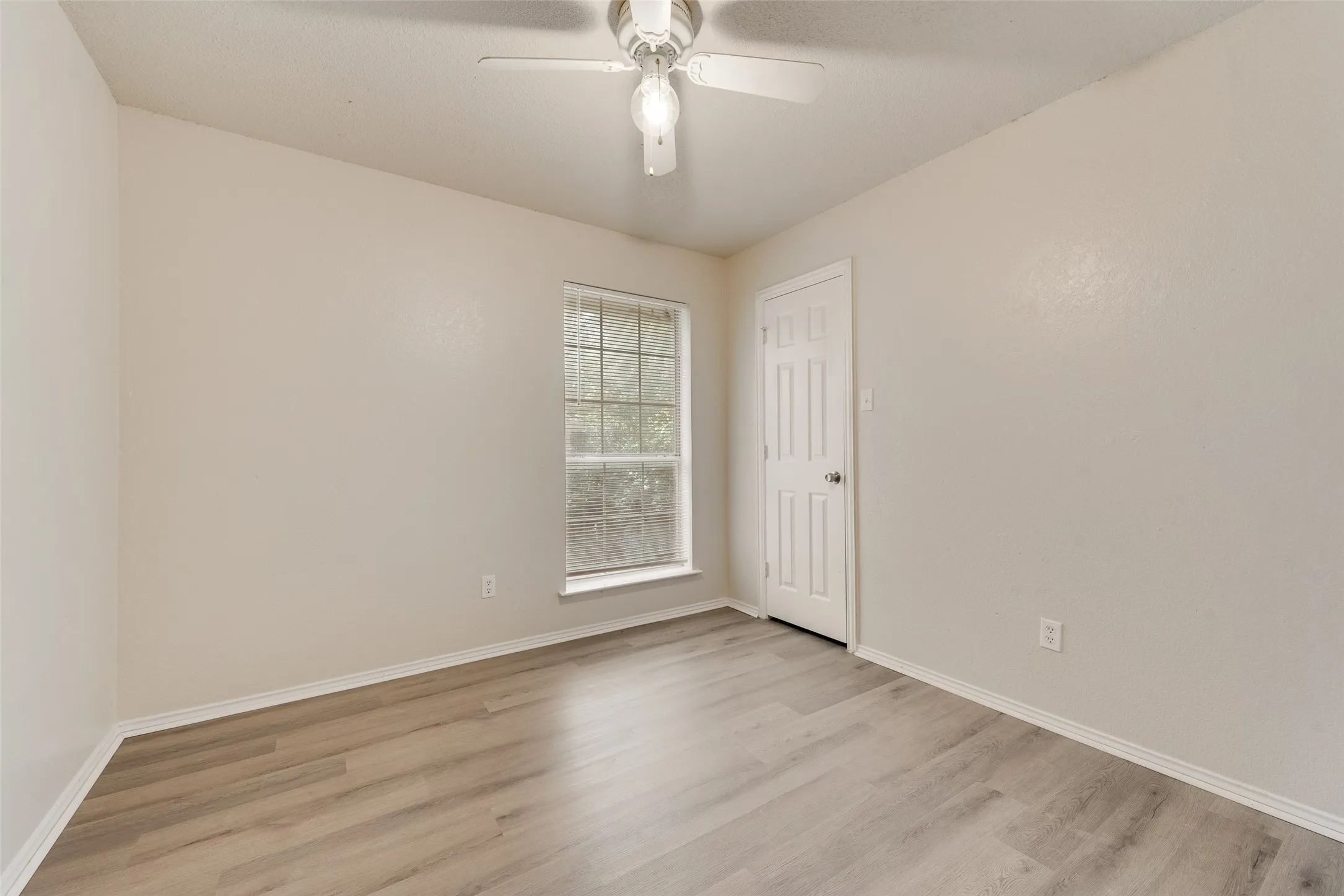 Wood-finish flooring, single window, paneled door, and a ceiling fan with light fixture