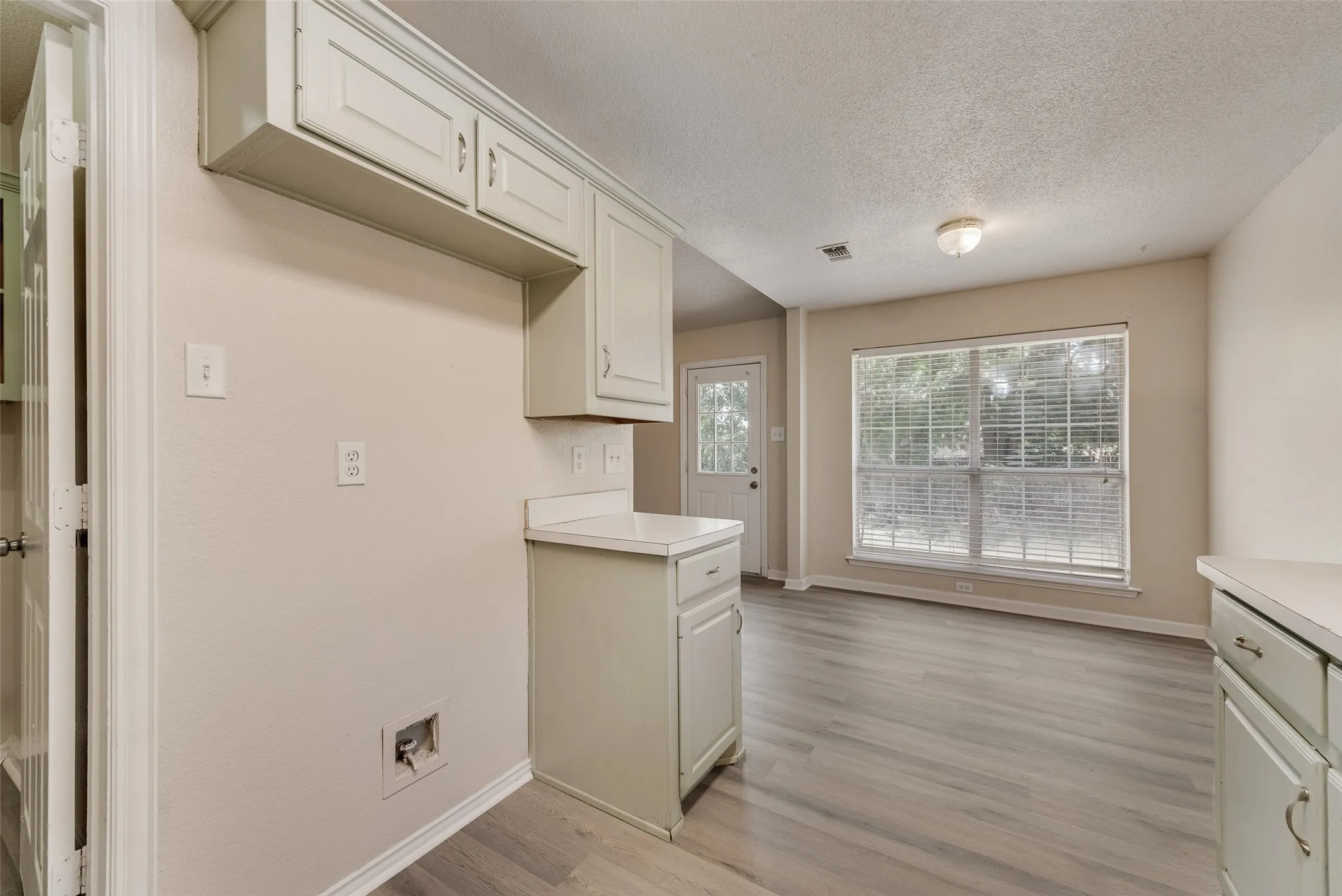 Light wood-finish flooring, recessed lighting, white cabinetry with silver hardware, white countertops, and a large window with blinds