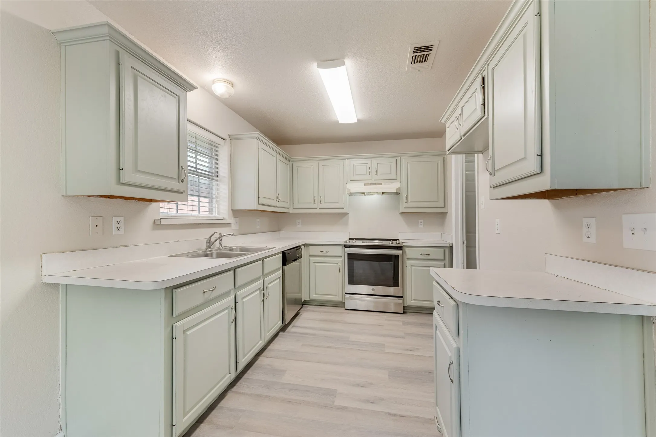 Kitchen featuring light-toned cabinetry, light-toned countertops, a stainless steel range, and wood-finish flooring