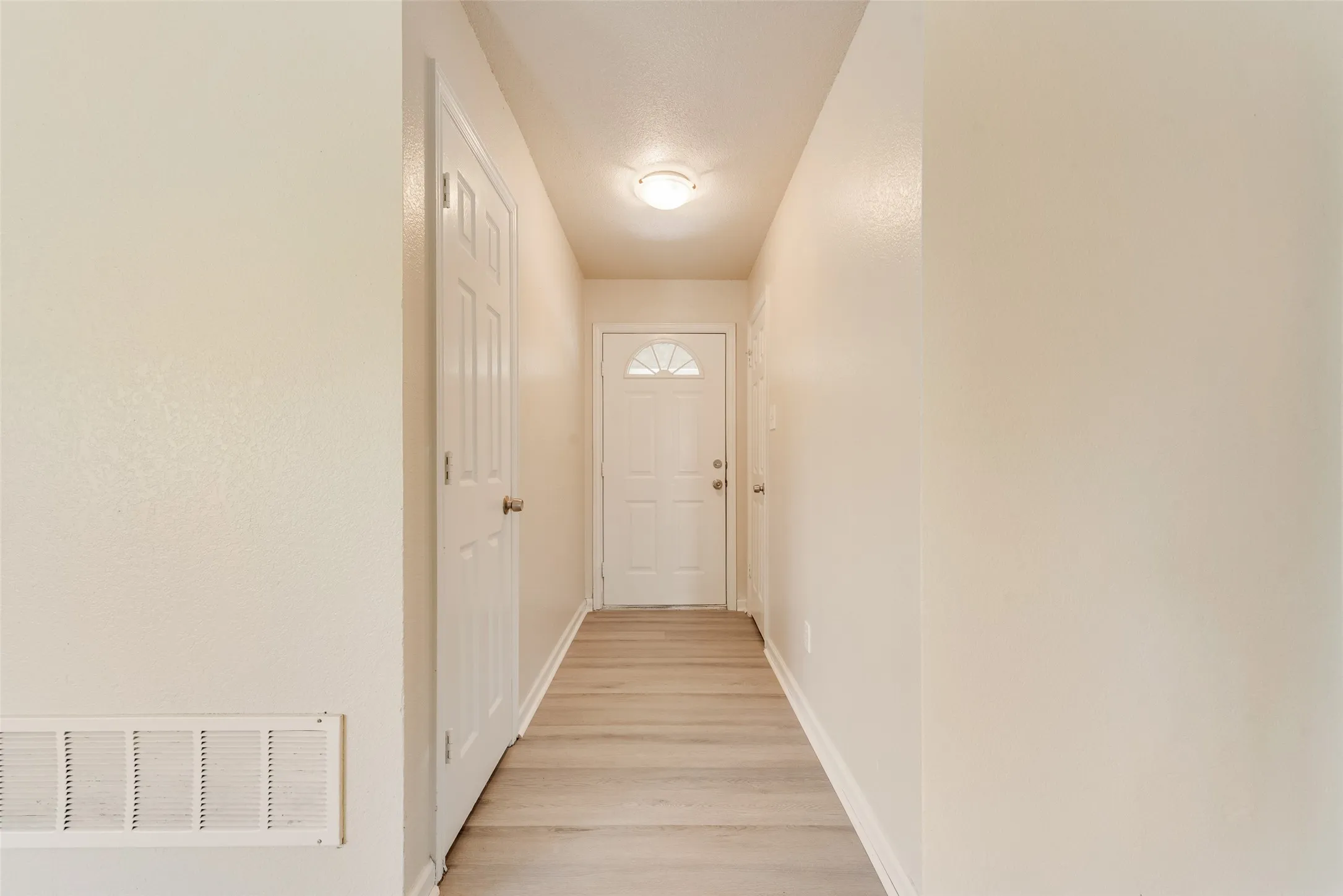 Hallway featuring neutral wall tones, wood-finish flooring, a paneled interior door, and a white exterior door with an arched glass insert