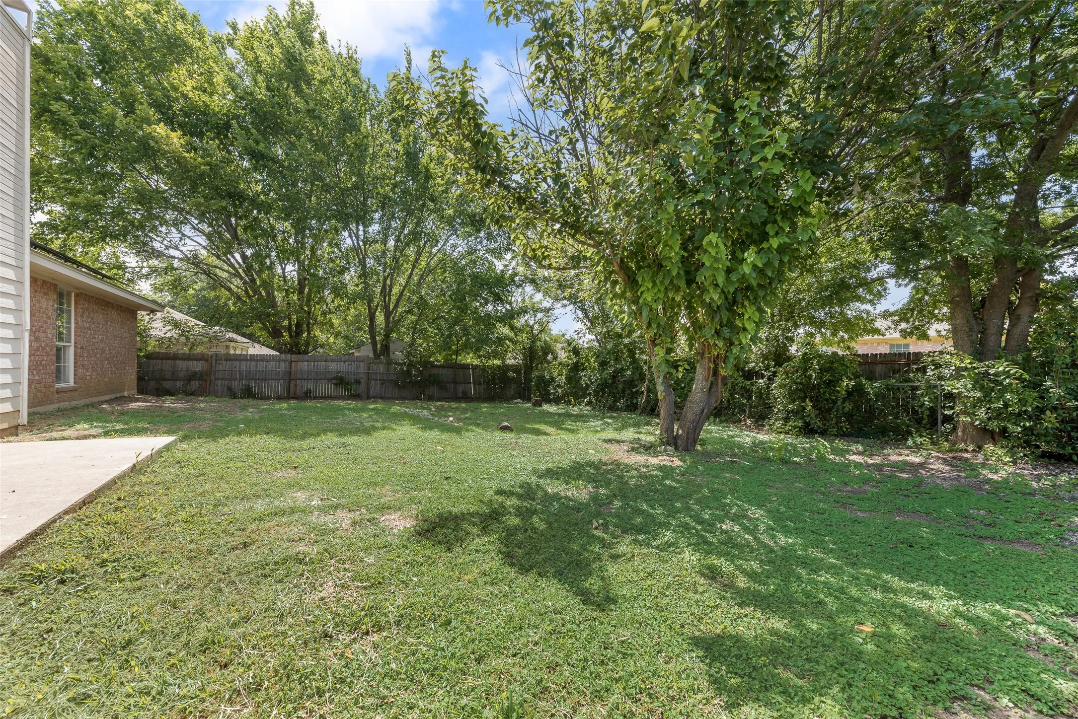 Expansive green lawn with mature trees providing natural shading, bordered by a wood fence