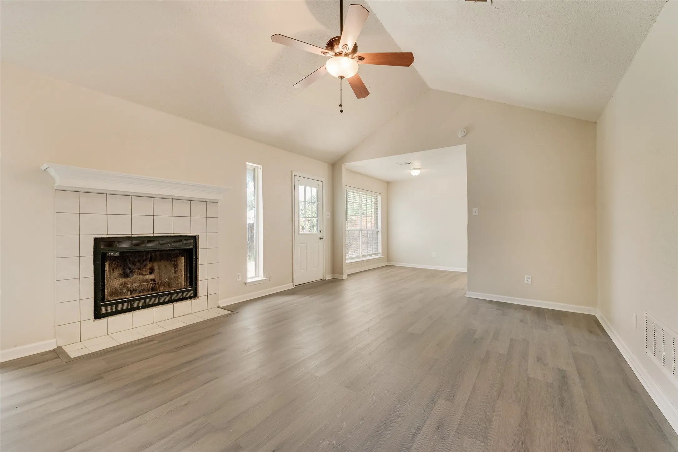 Vaulted ceiling with an attached ceiling fan, a tiled fireplace, and wood-finish flooring