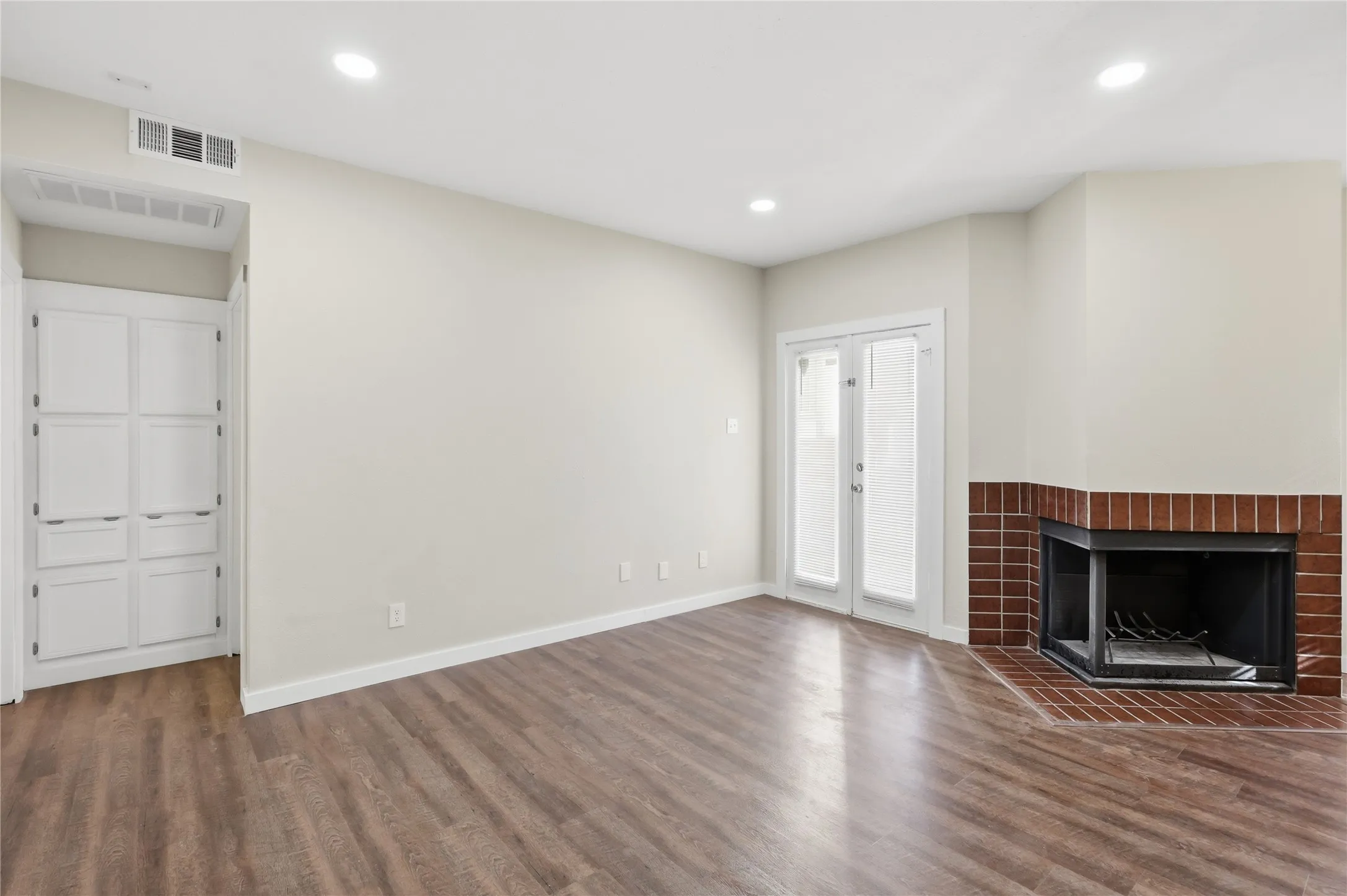 Wood-finish flooring, recessed lighting, built-in cabinetry, French doors, and a brick-surround fireplace