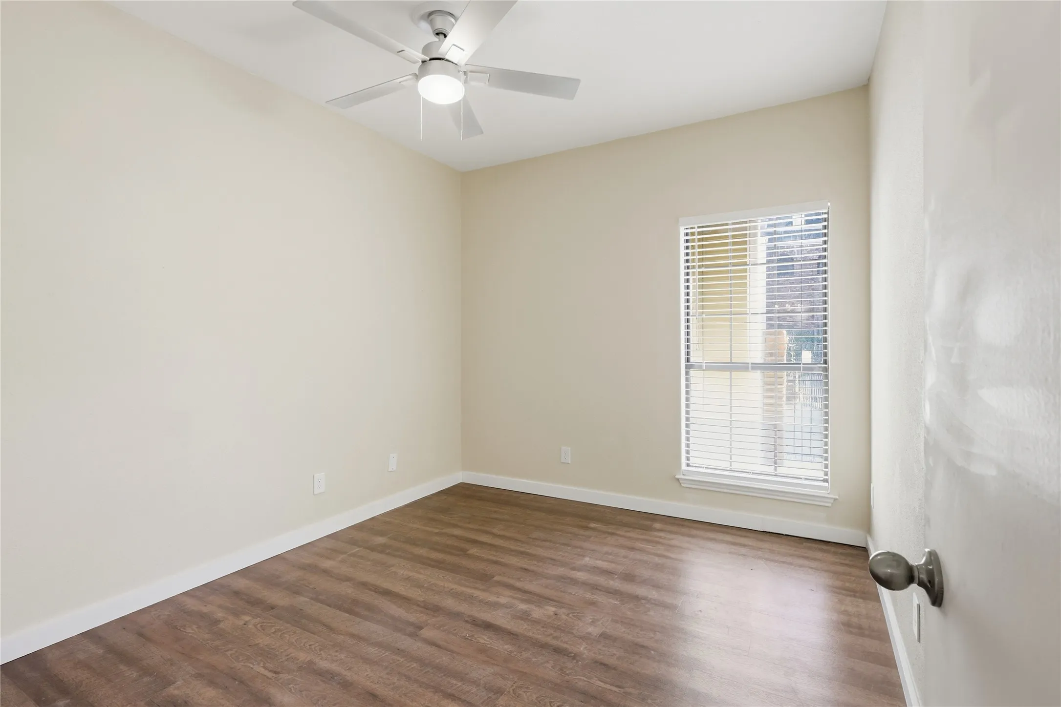 Wood-finish flooring with white baseboards, a ceiling fan with integrated lighting, and a window with blinds